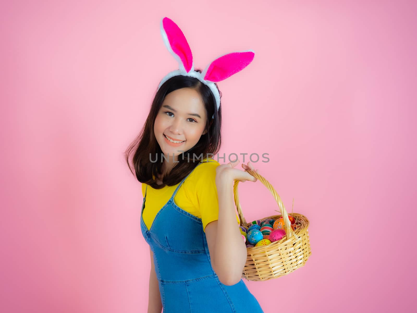 Portrait of a happy young woman wearing Easter bunny ears prepares to celebrate Easter on a pink background.