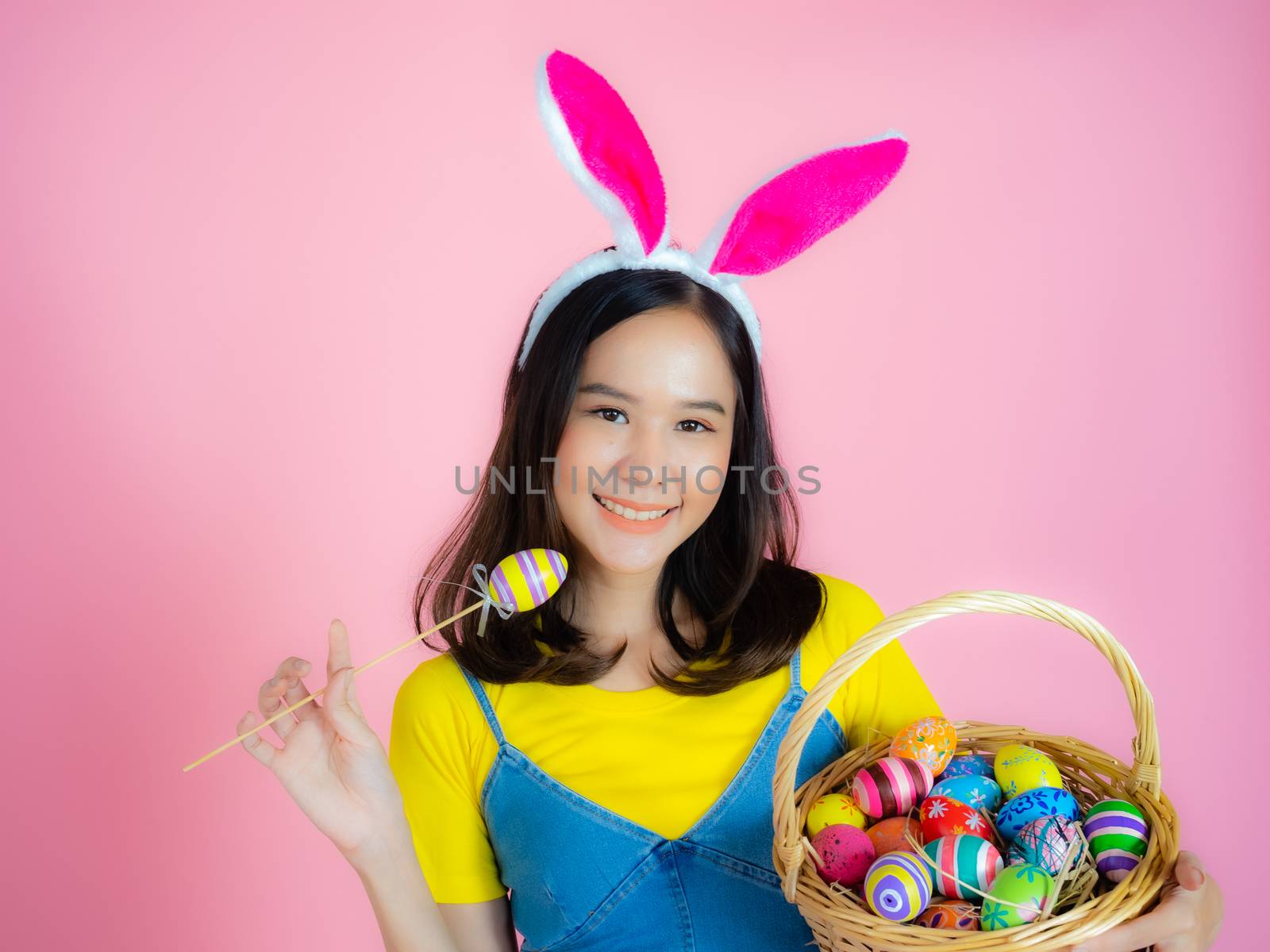 Portrait of a happy young woman wearing Easter bunny ears prepares to celebrate Easter on a pink background.