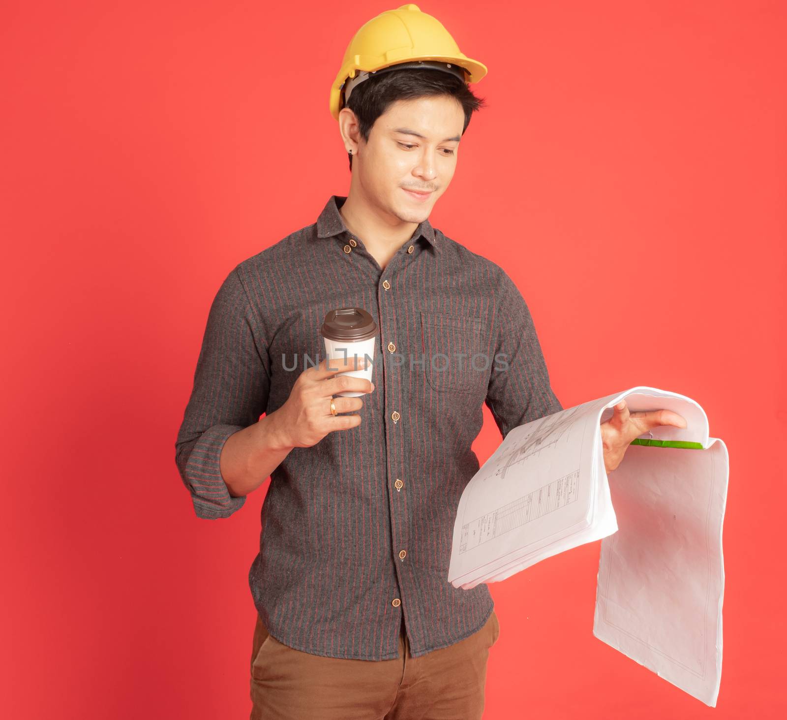 The young civil engineer is considering the construction plan while enjoying coffee. Portrait people concept on red background