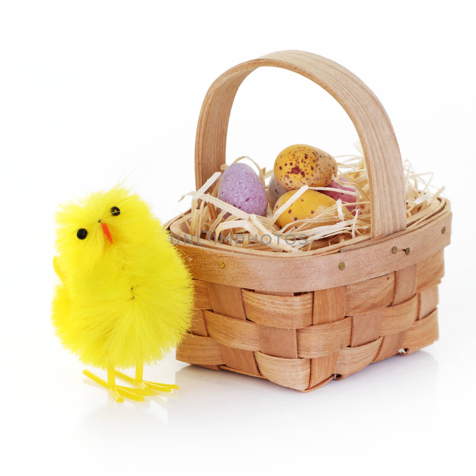 An Easter chick and candy eggs in a basket with straw on white