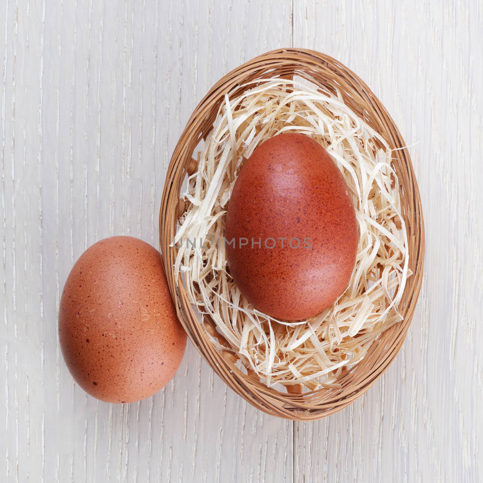 Brown chicken eggs on light wood with basket and straw