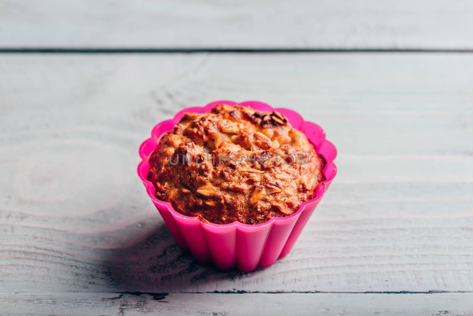 Cooked oatmeal muffin in a pink silicone bakeware over light wooden background.