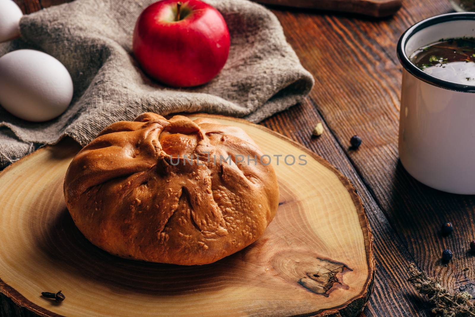 Rustic breakfast with traditional tatar pastry elesh, herbal tea in metal mug, apple and boiled eggs over dark wooden surface