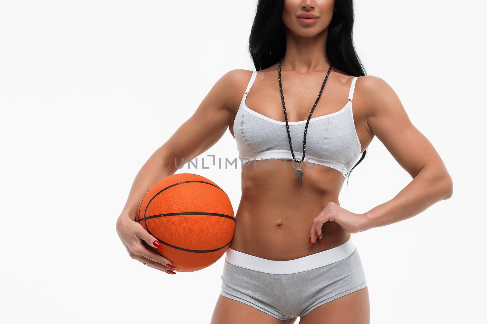 Beautiful slim sexual woman in underwear with whistle holding basketball ball and looking at camera on white background