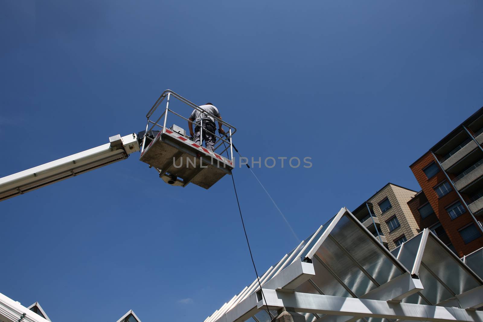 worker of Professional Facade Cleaning Services washing a glass roof with blue sky