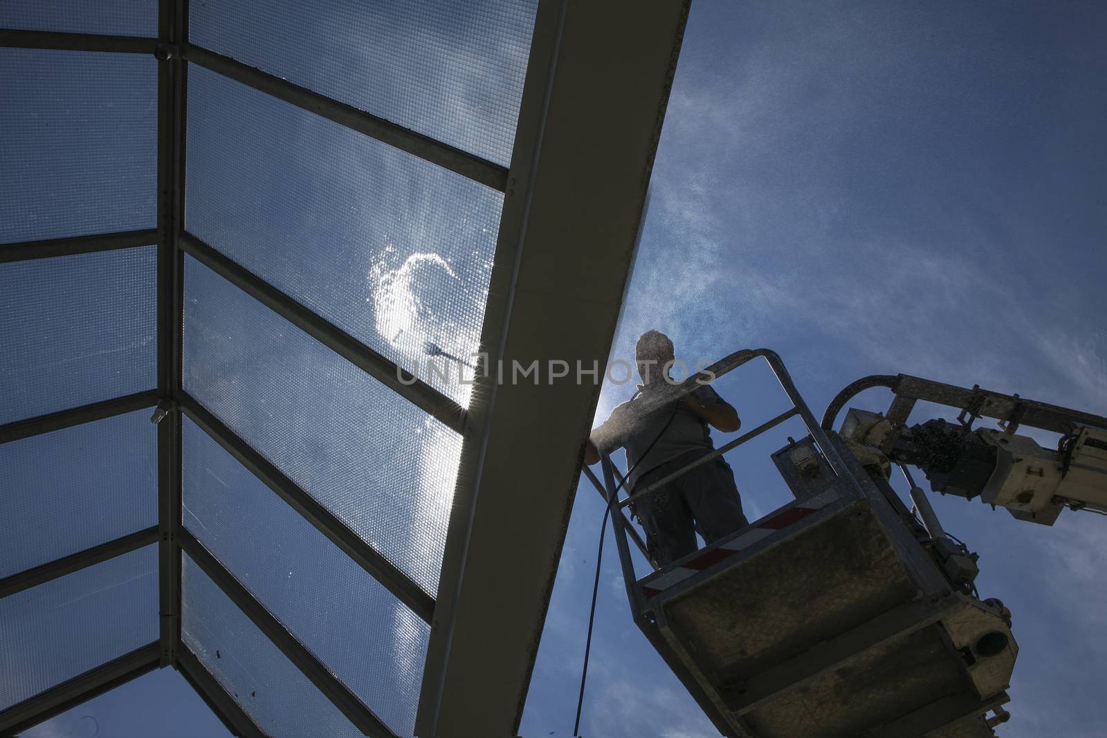 worker of Professional Facade Cleaning Services washing a glass roof with blue sky