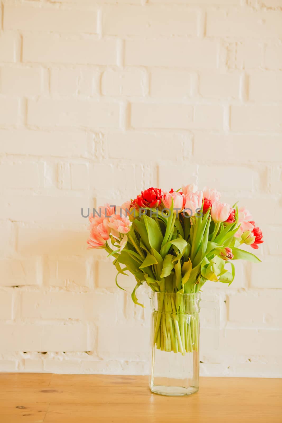 Glass vase with bouquet of beautiful tulips on brick wall background.