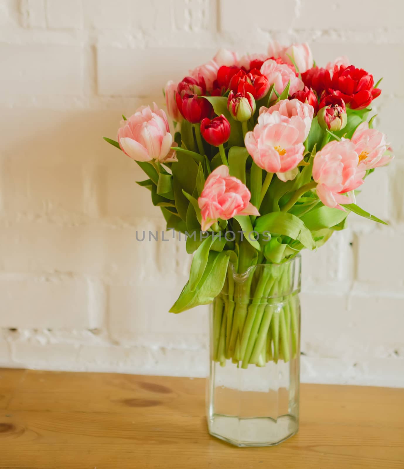Glass vase with bouquet of beautiful tulips on brick wall background.