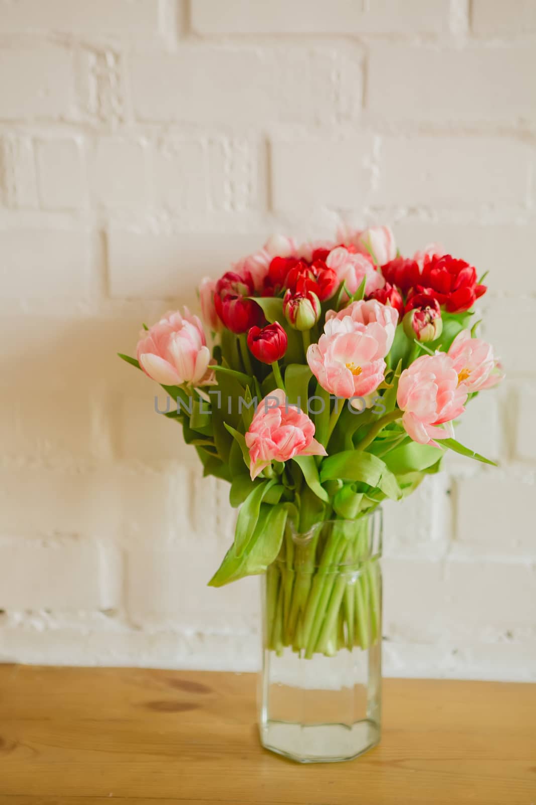 Glass vase with bouquet of beautiful tulips on brick wall background.