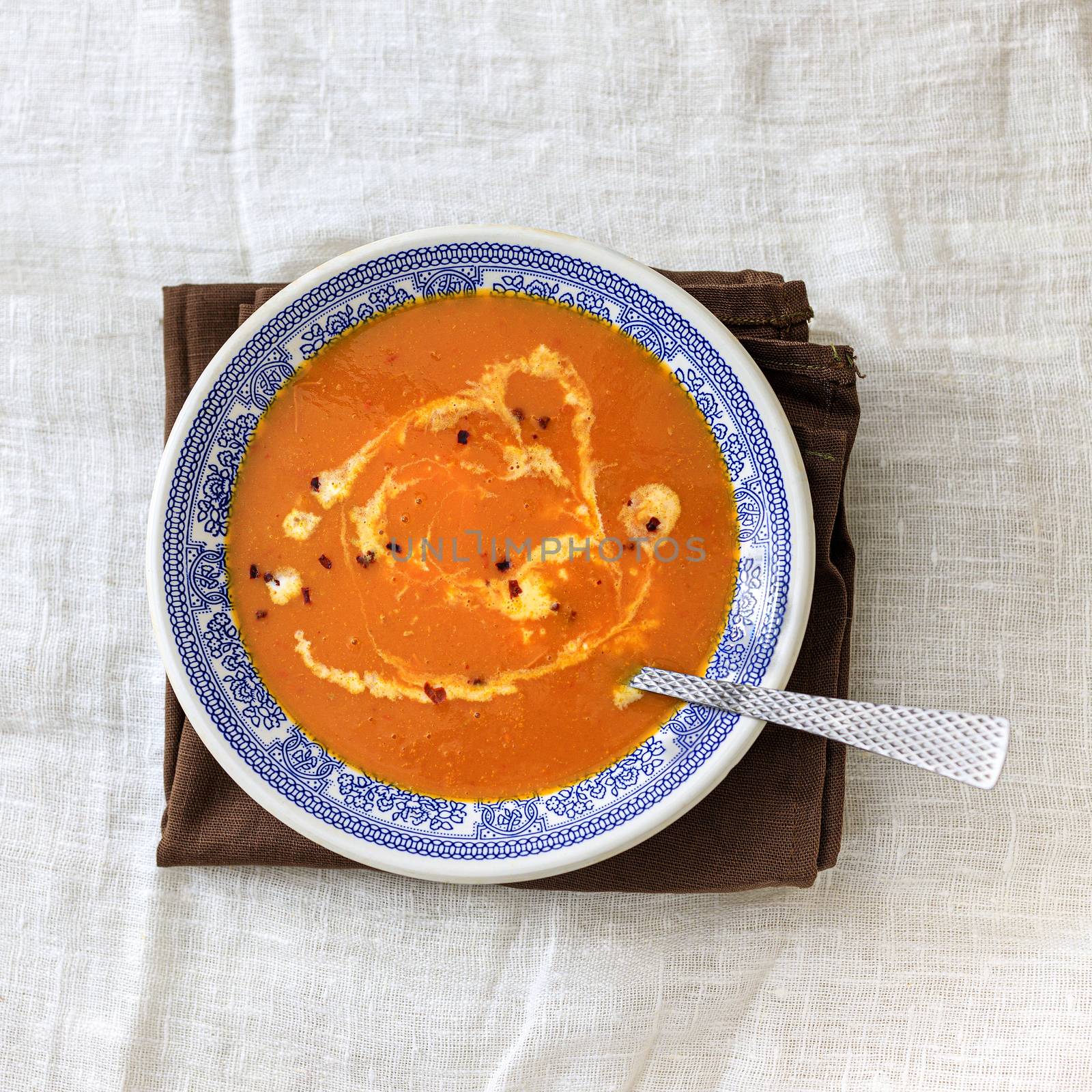 Orange pumpkin puree soup with smerana and red chili peppers in a plate with a blue traditional Moroccan pattern on a plain white background. Flat lay. Top view, copy space