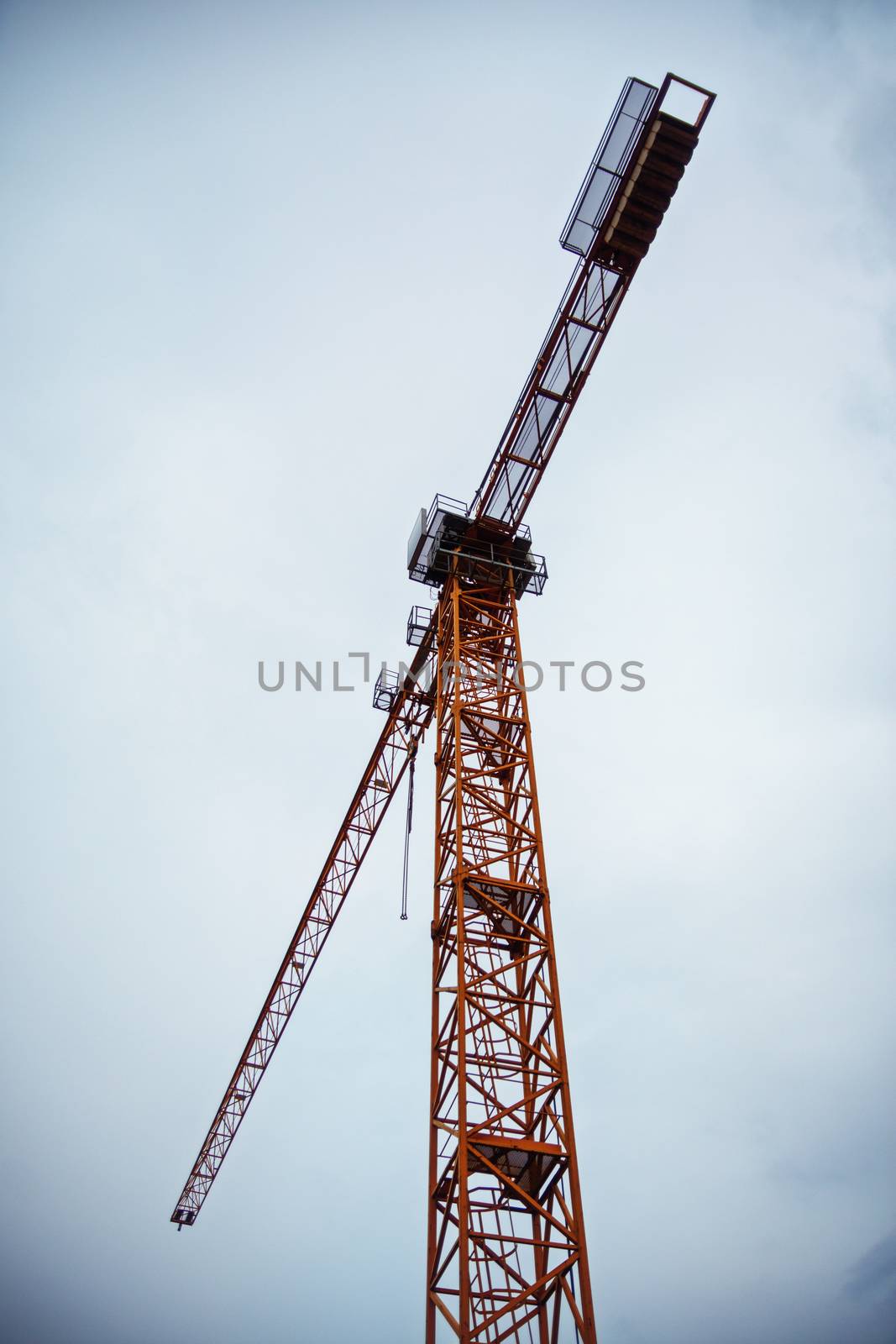 Bottom up view of a big tower crane against a cloudy sky. Background image of construction equipment. Copy space.