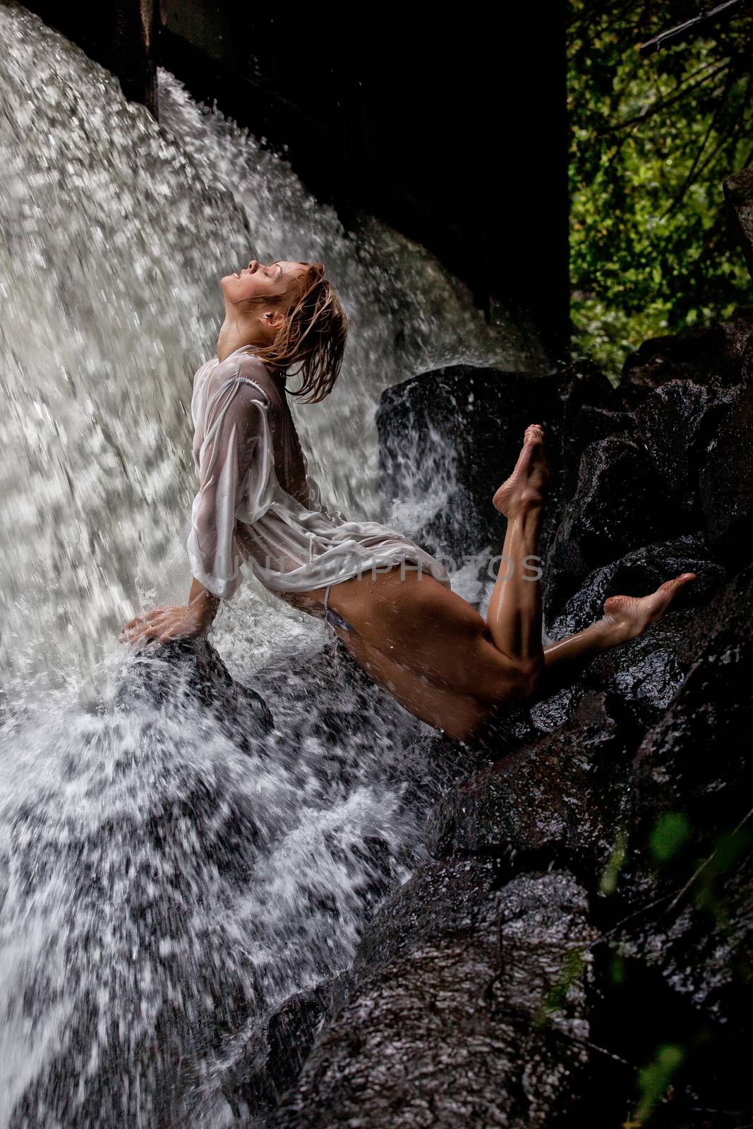 Young blonde woman in a white shirt swimming in a waterfall