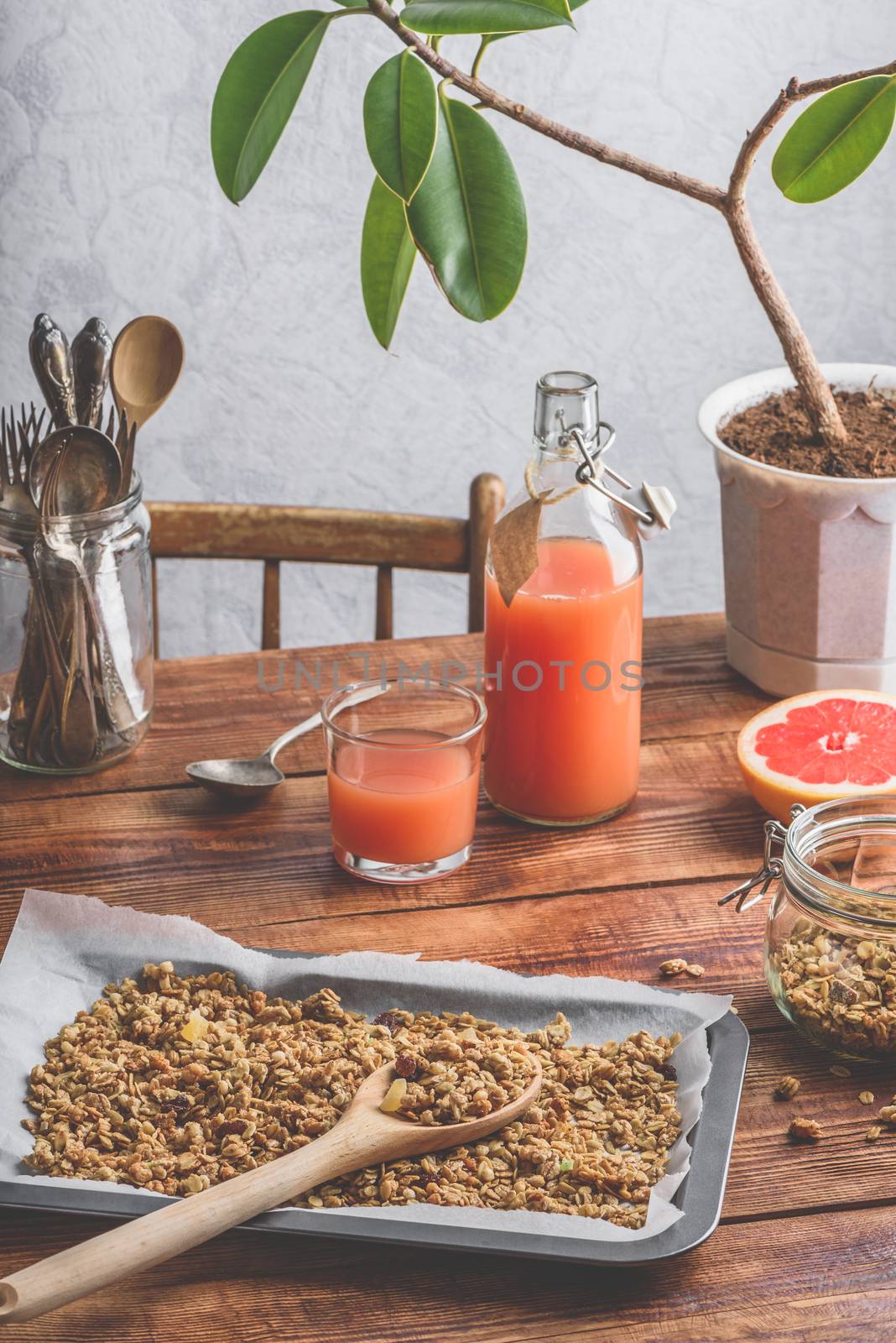 Homemade granola on baking sheet with wooden spoon,  grapefruit juice and sliced fruit