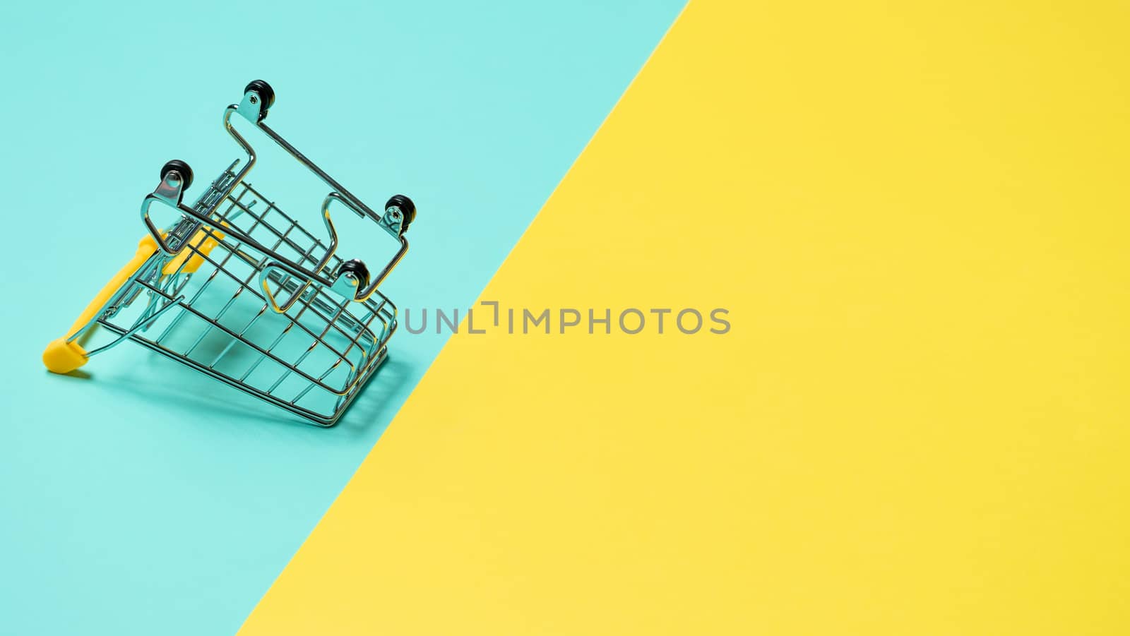 Empty inverted shopping cart on blue and yellow background. Inverted toy trolley on bright colorful background, copy space for text or design.