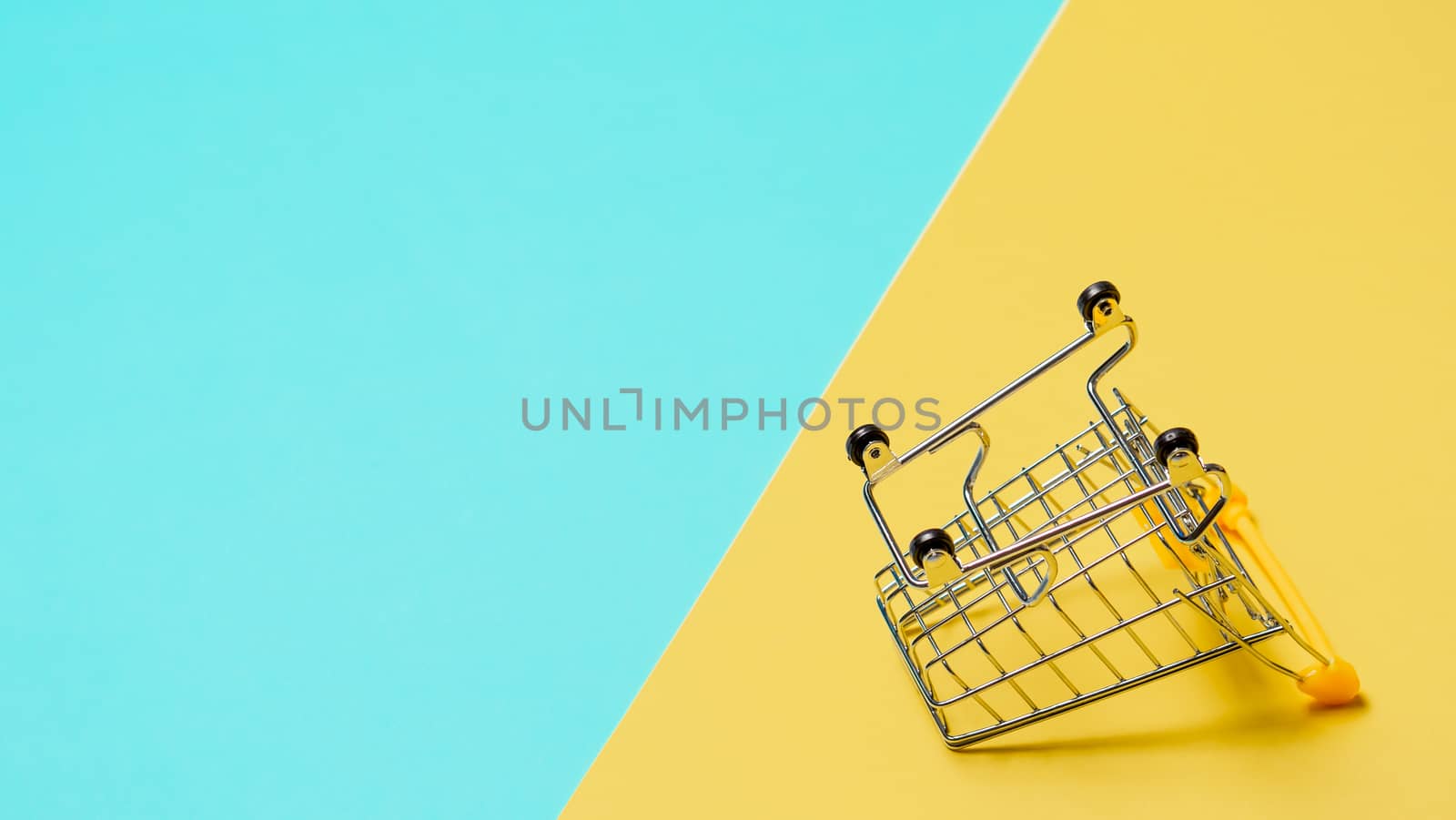 Empty inverted shopping cart on blue and yellow background. Inverted toy trolley on bright colorful background, copy space for text or design.