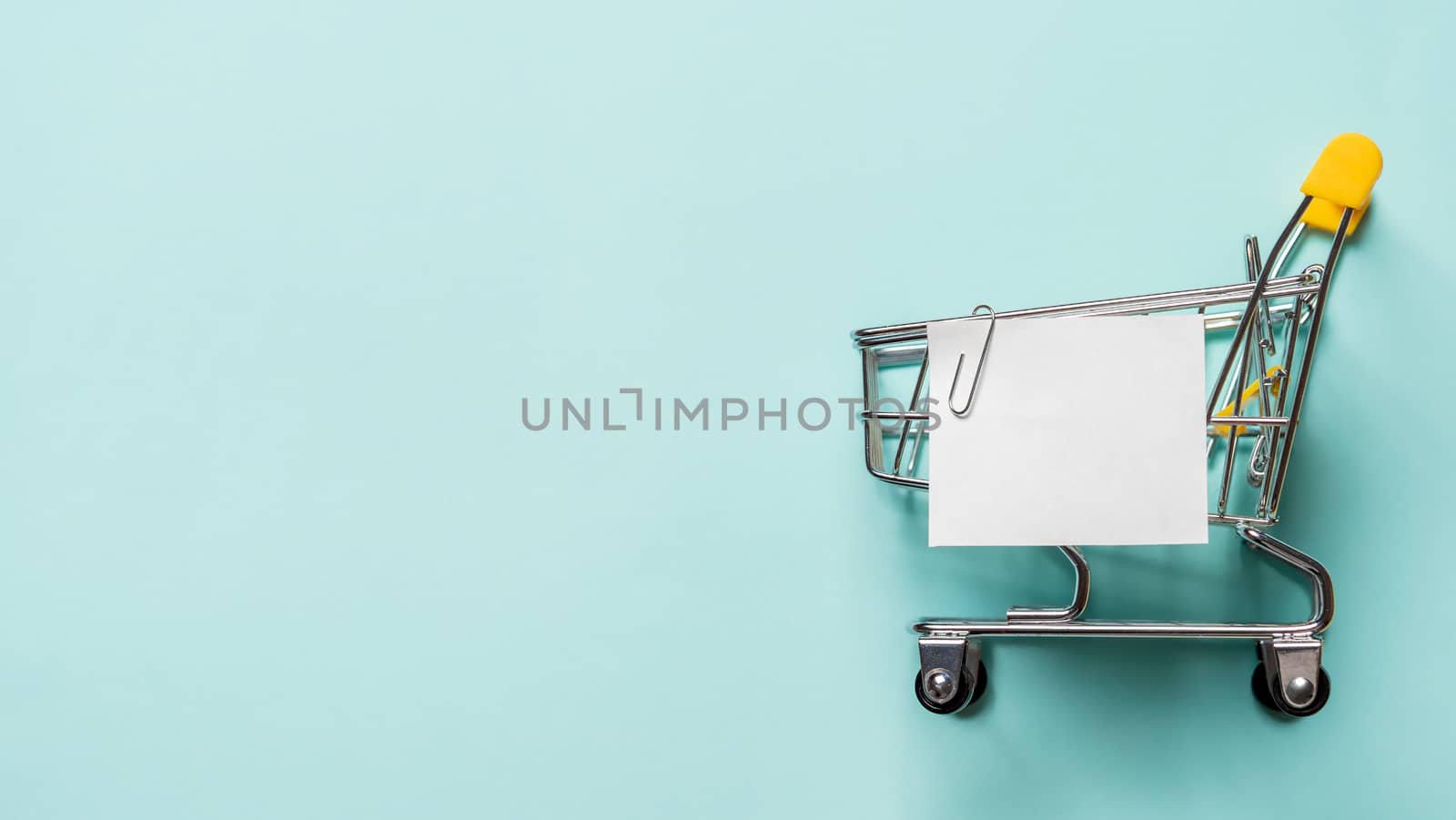 Shopping cart and white paper note list over blue background. Shopping concept on blue background. Empty white paper note over shopping cart. Copy space for text or design. Banner