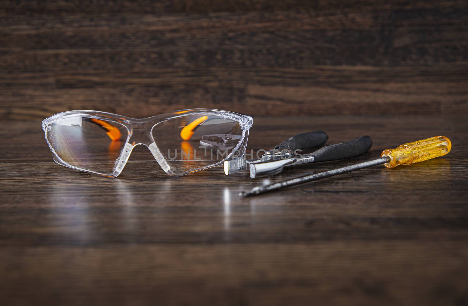 protective glasses, pliers and a screw driver against a dark wood background