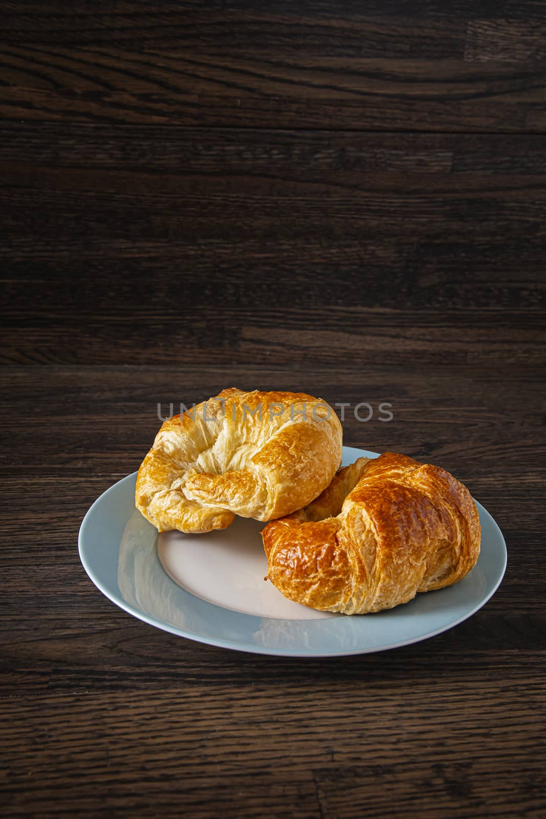 two croissant on a plate against a dark wood background