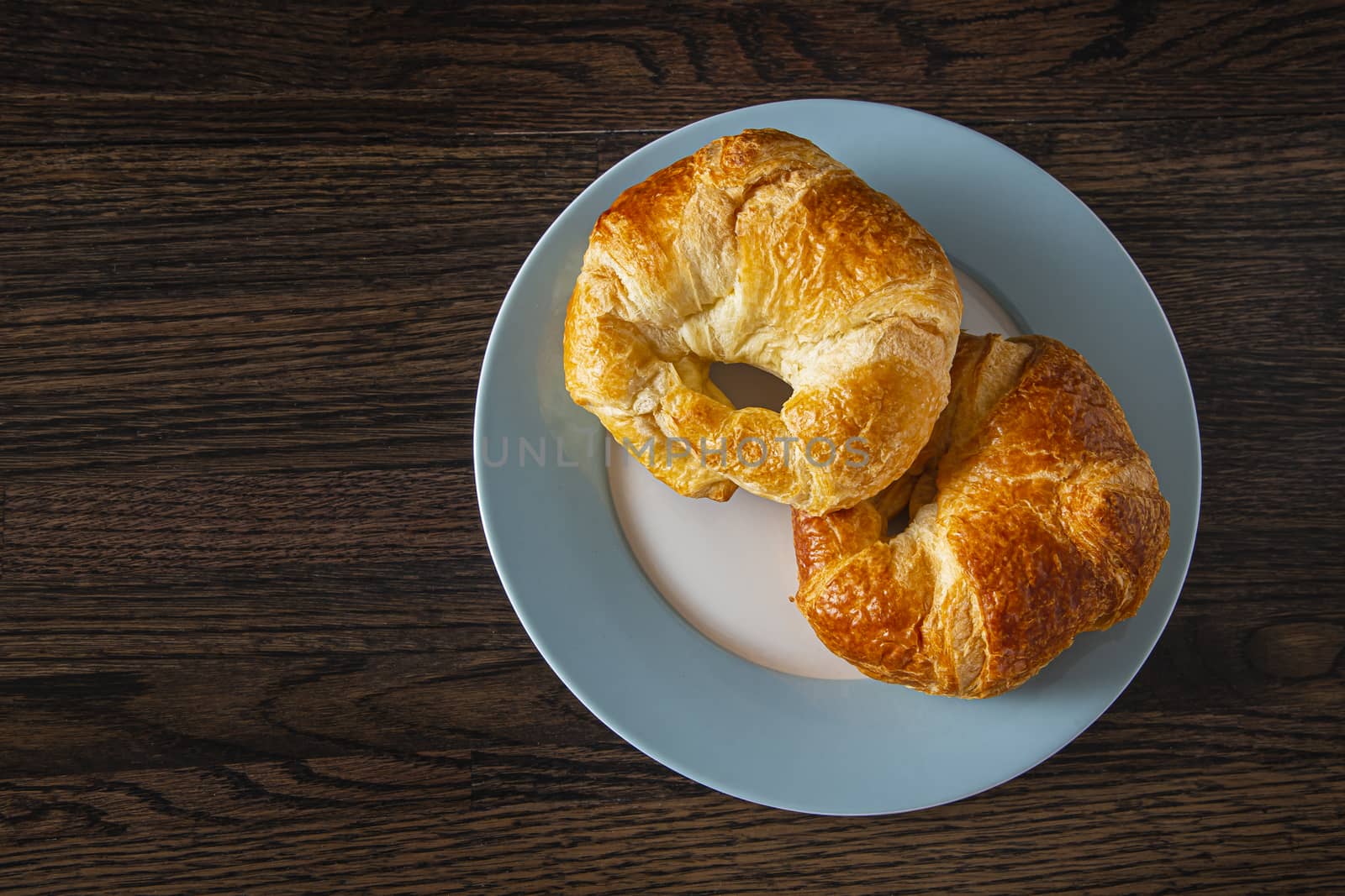top view of two croissant on a plate against a wood background