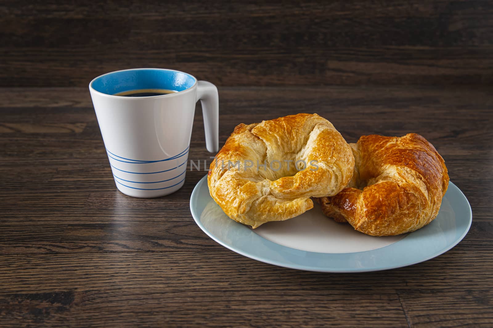 black coffee and two croissant against a dark wood background