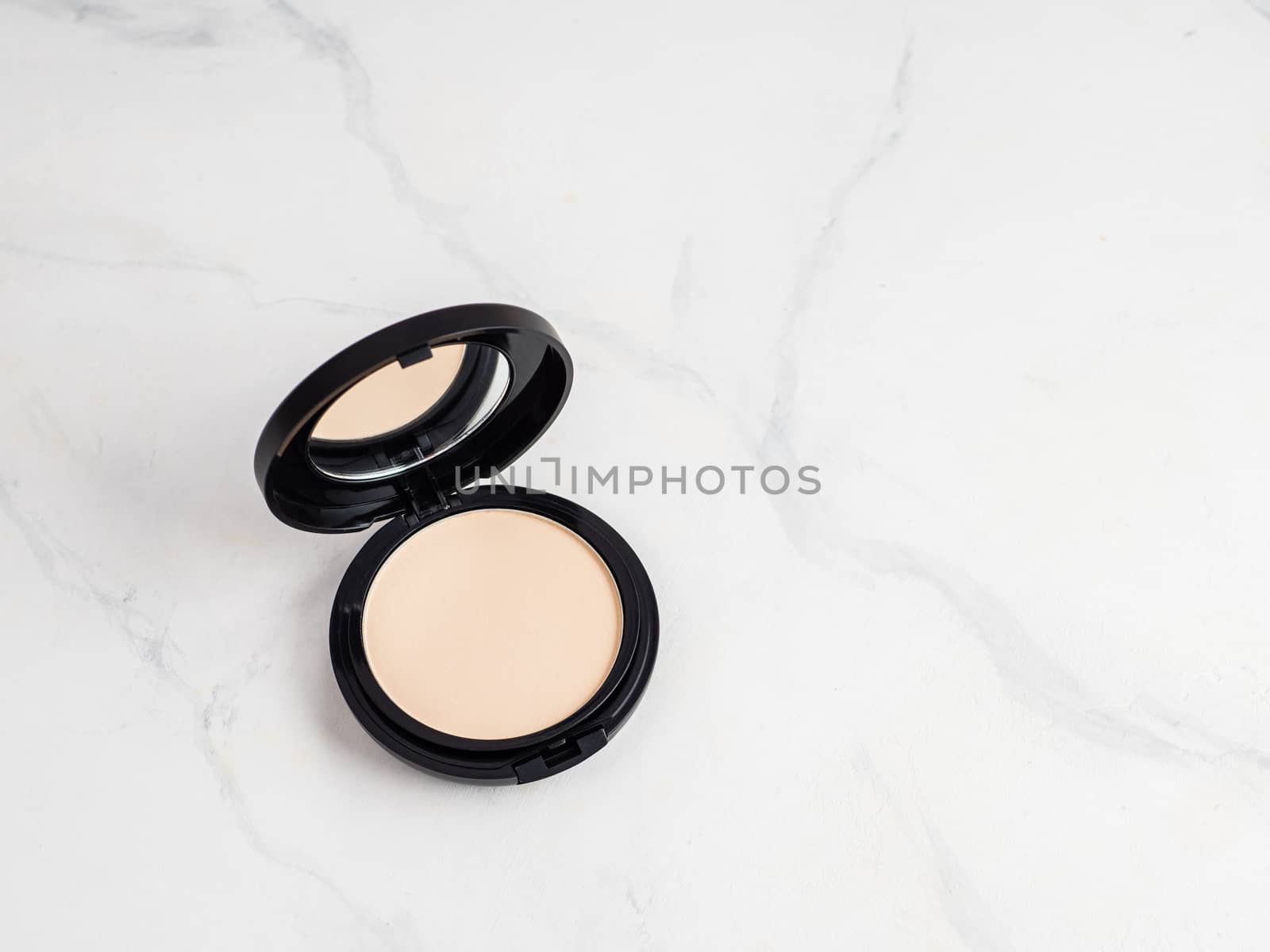 Compact powder on white marble background. Female pressed powder in opened black plastic case with mirror, copy space for text or design. Top view or flat lay