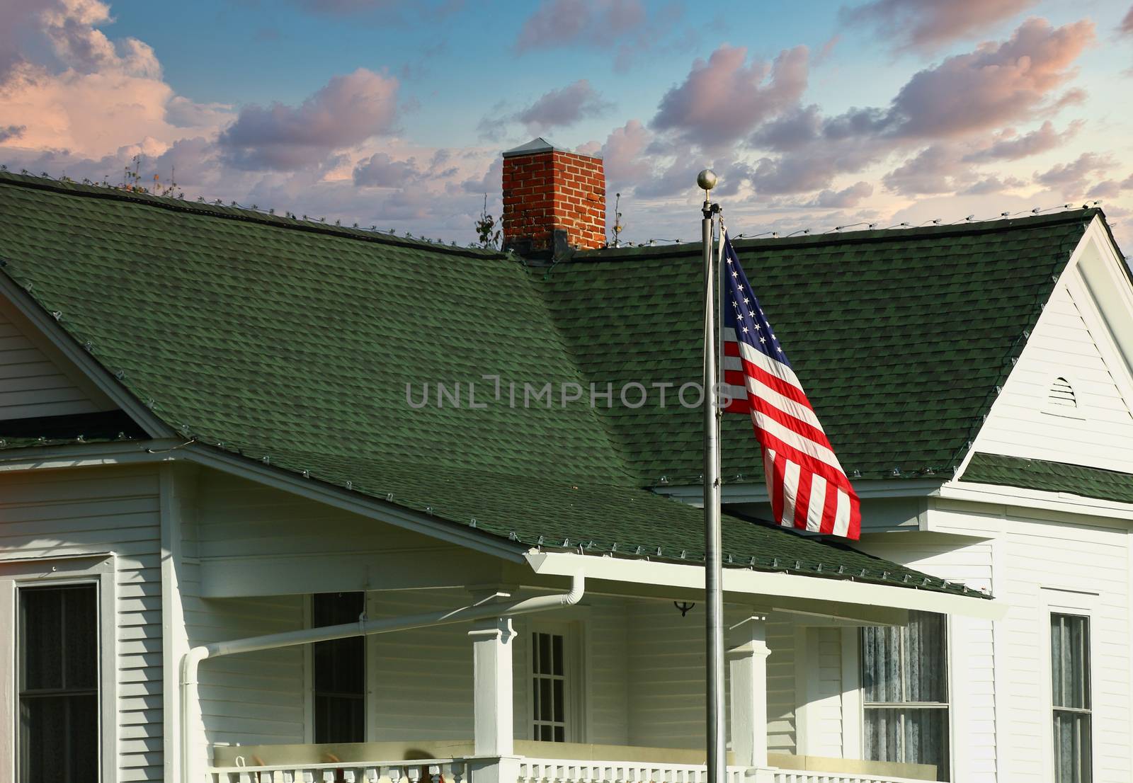 An old house with green shingled roof and an American flag