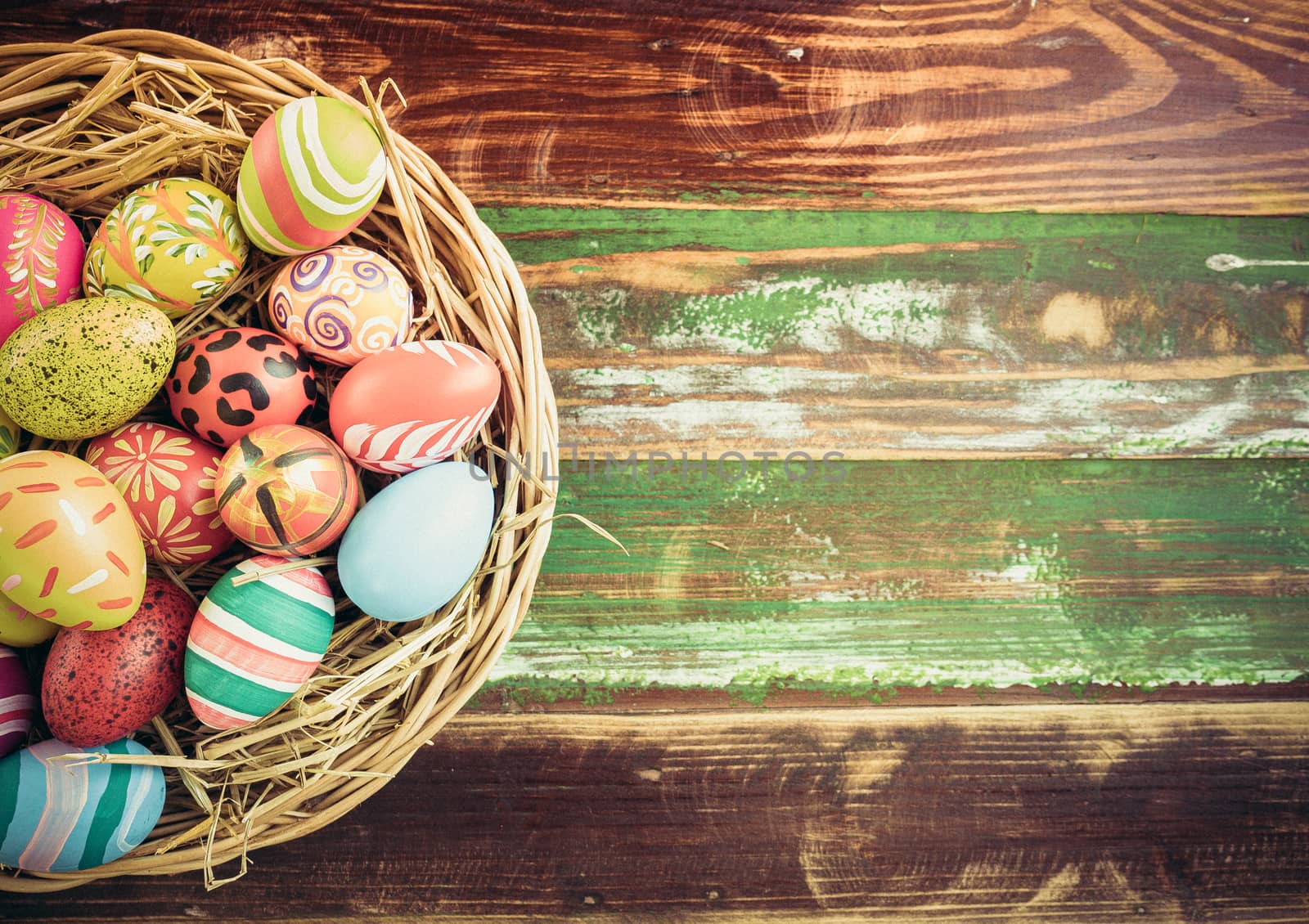 Easter eggs in various patterns and colors in a bird's nest placed on a wooden floor decorated in retro style.