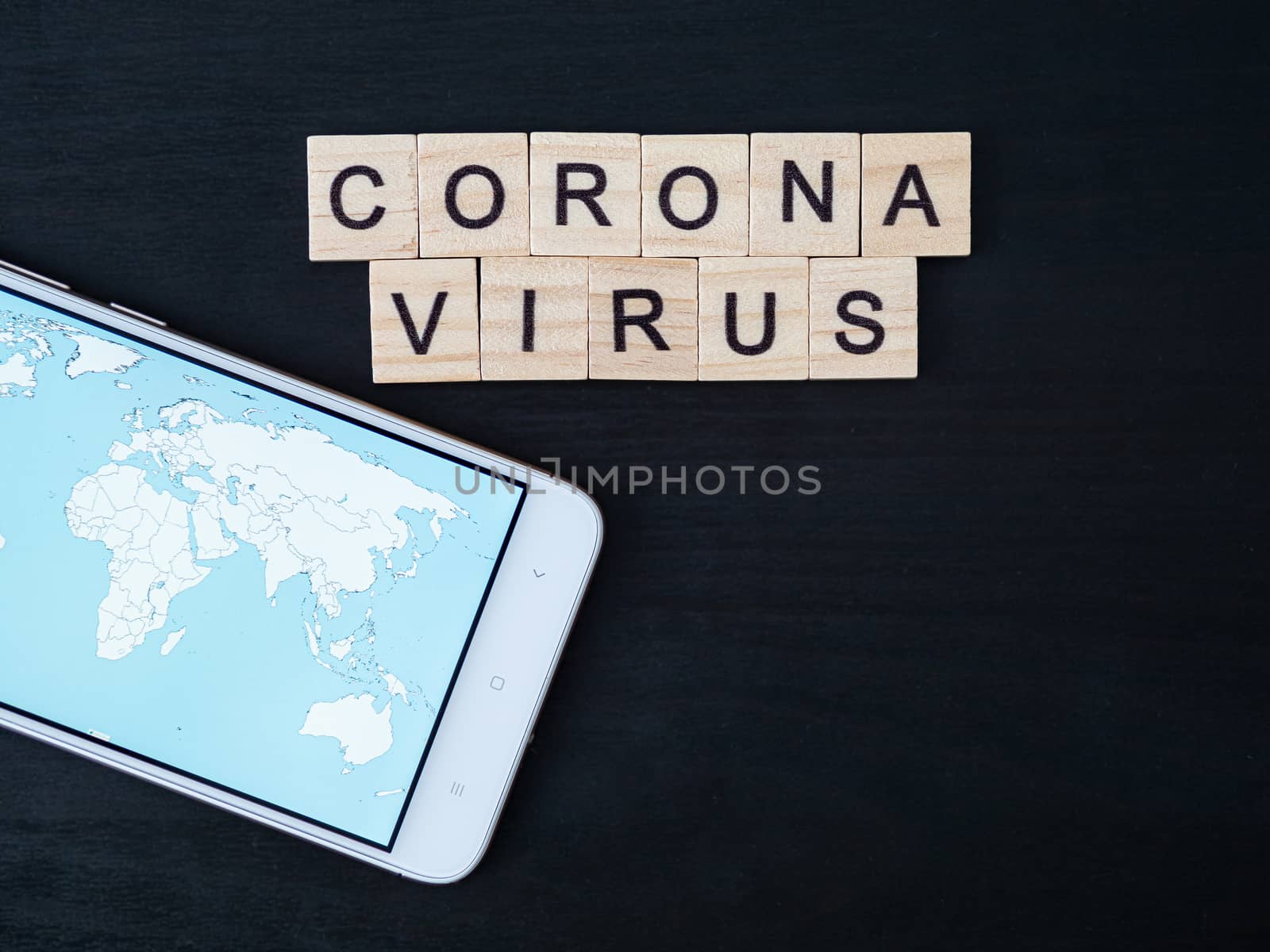 Coronavirus word made of wood block and world map on smartphone screen. Coronavirus text on dramatic atmosphere black wooden table. Coronavirus concept top view, copy space