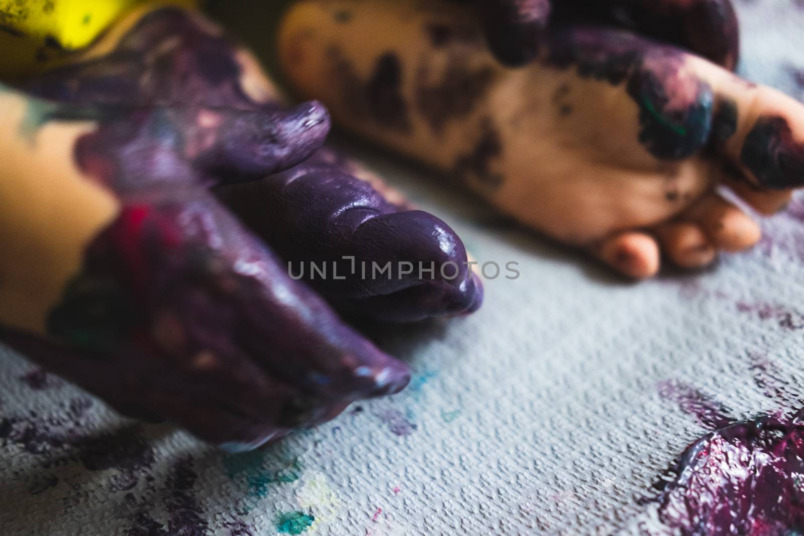 Chlid playing with different color paintings ends with multicolor hands and feet