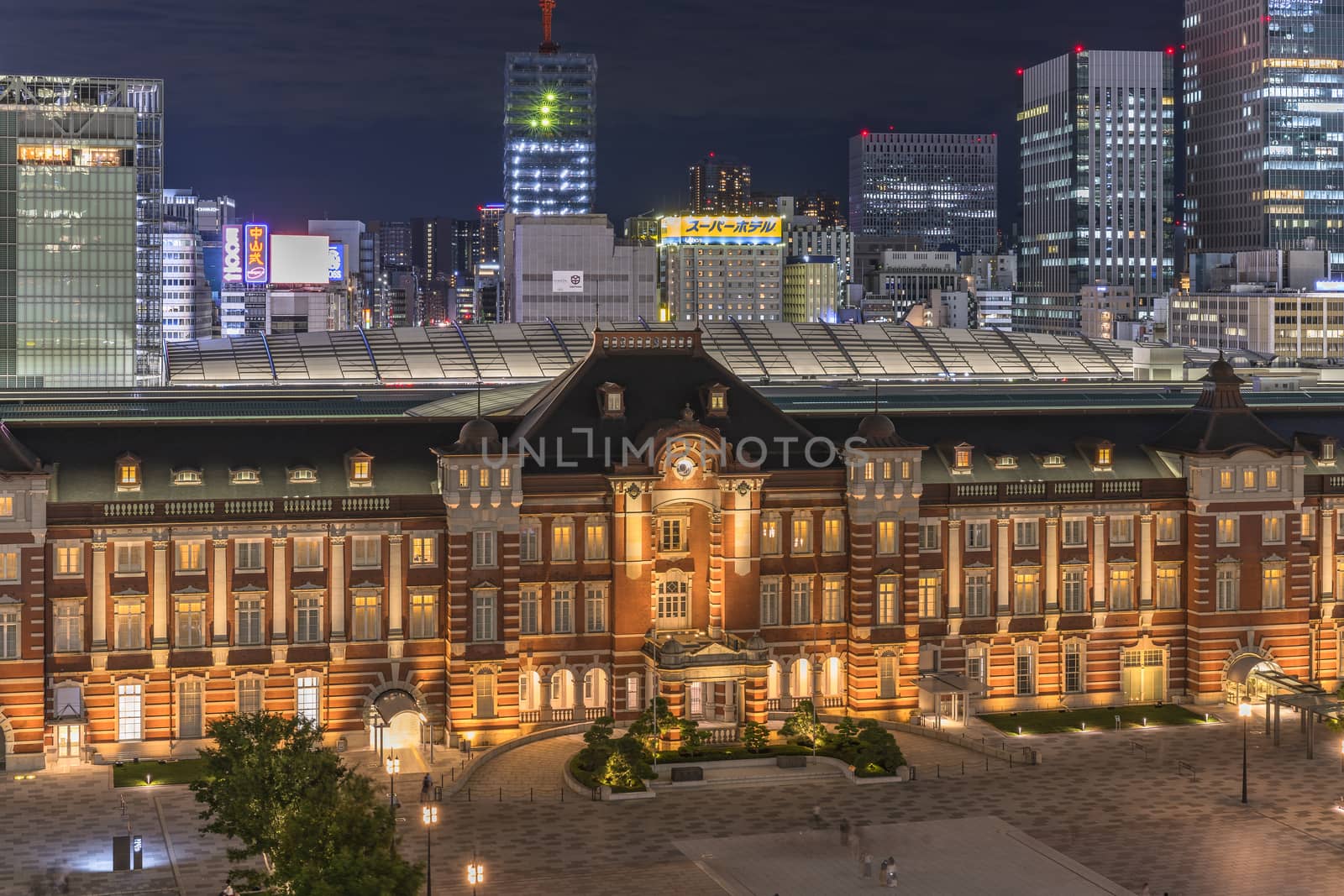 Night view of Marunouchi side of Tokyo railway station in the Chiyoda City, Tokyo, Japan.  The station is divided into Marunouchi and Yaesu sides in its directional signage. The station first called Central Station was built in 1914 directly in front of the Imperial Palace gardens. The three-story station building was designed by architect Tatsuno Kingo who also designed Manseibashi Station and the nearby Bank of Japan building. Much of the station was destroyed in B-29 firebombing on May 25, 1945. The bombing shattered the impressive rooftop domes. The station was quickly rebuilt within the year, but simple angular roofs were built in place of the domes, and the restored building was only two stories tall instead of three. 