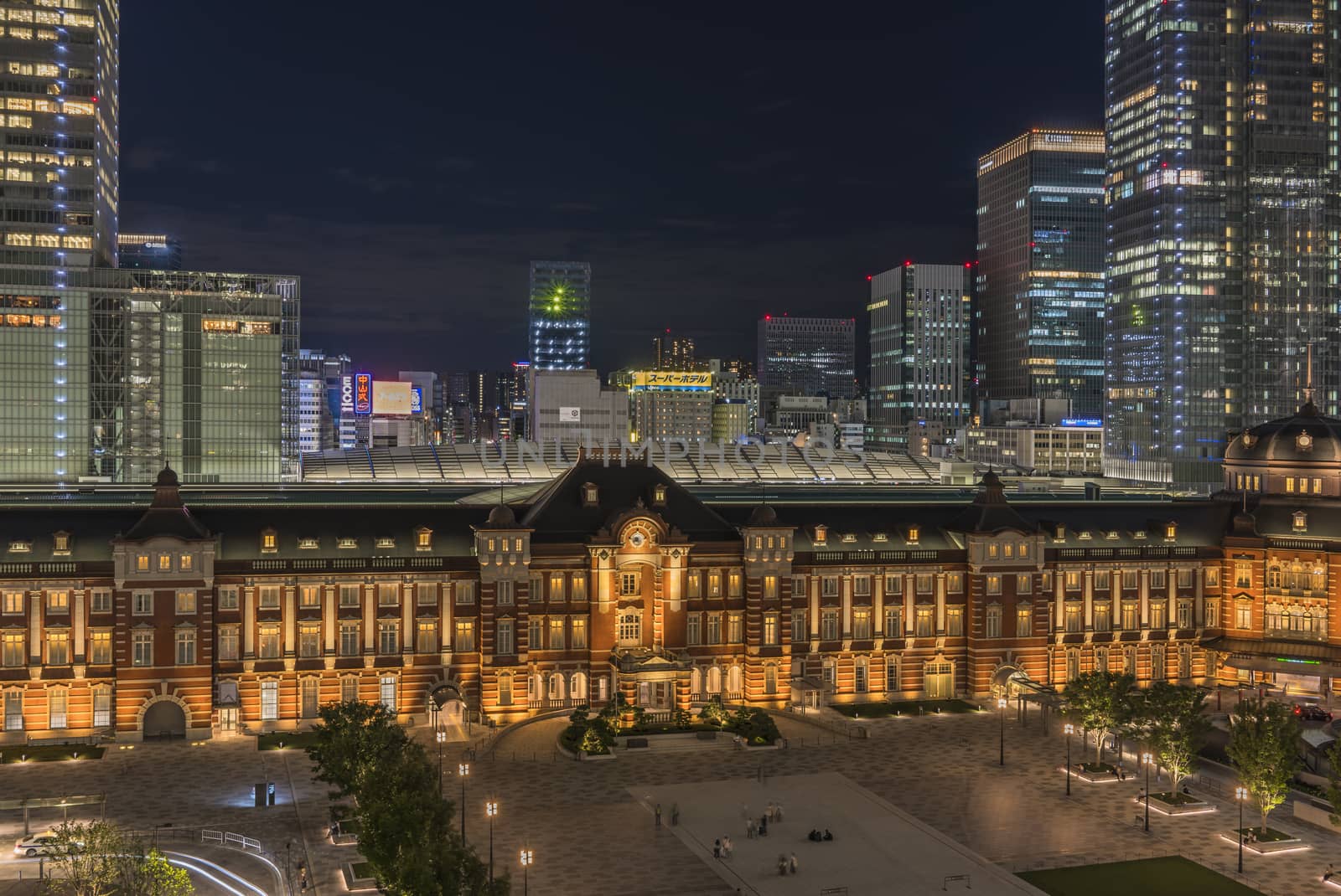 Night view of Marunouchi side of Tokyo railway station in the Chiyoda City, Tokyo, Japan.  The station is divided into Marunouchi and Yaesu sides in its directional signage. The station first called Central Station was built in 1914 directly in front of the Imperial Palace gardens. The three-story station building was designed by architect Tatsuno Kingo who also designed Manseibashi Station and the nearby Bank of Japan building. Much of the station was destroyed in B-29 firebombing on May 25, 1945. The bombing shattered the impressive rooftop domes. The station was quickly rebuilt within the year, but simple angular roofs were built in place of the domes, and the restored building was only two stories tall instead of three. 