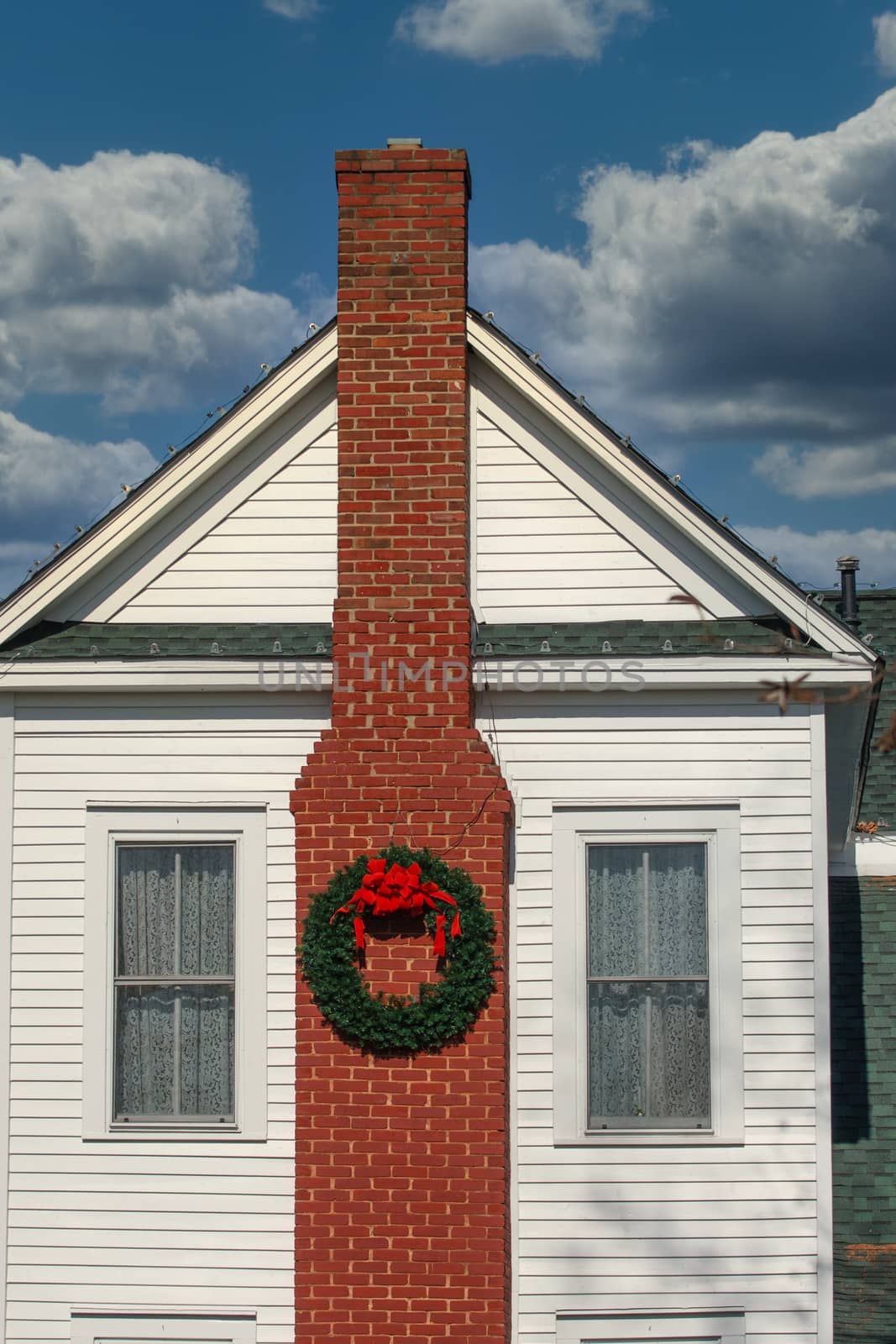Chirstmas Wreath with Red bow on a brick chimney of old white siding traditional farmhouse