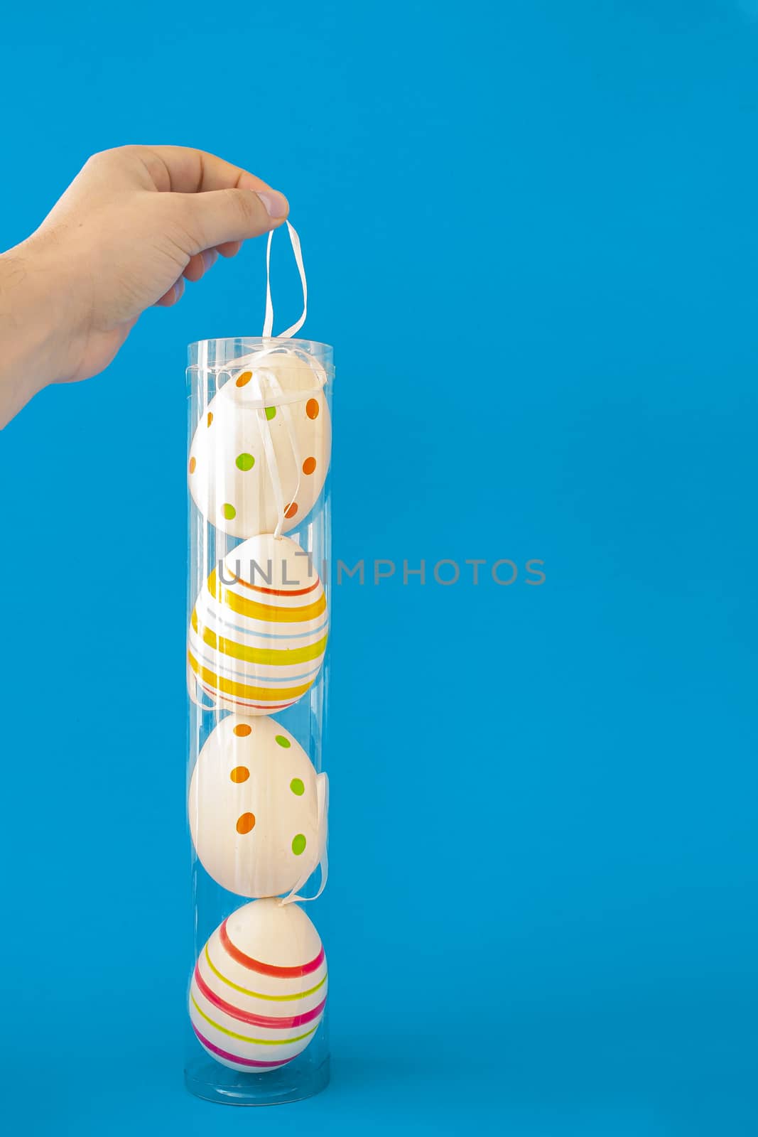A Person holding a container of colorful Easter eggs with a hanger on a blue background
