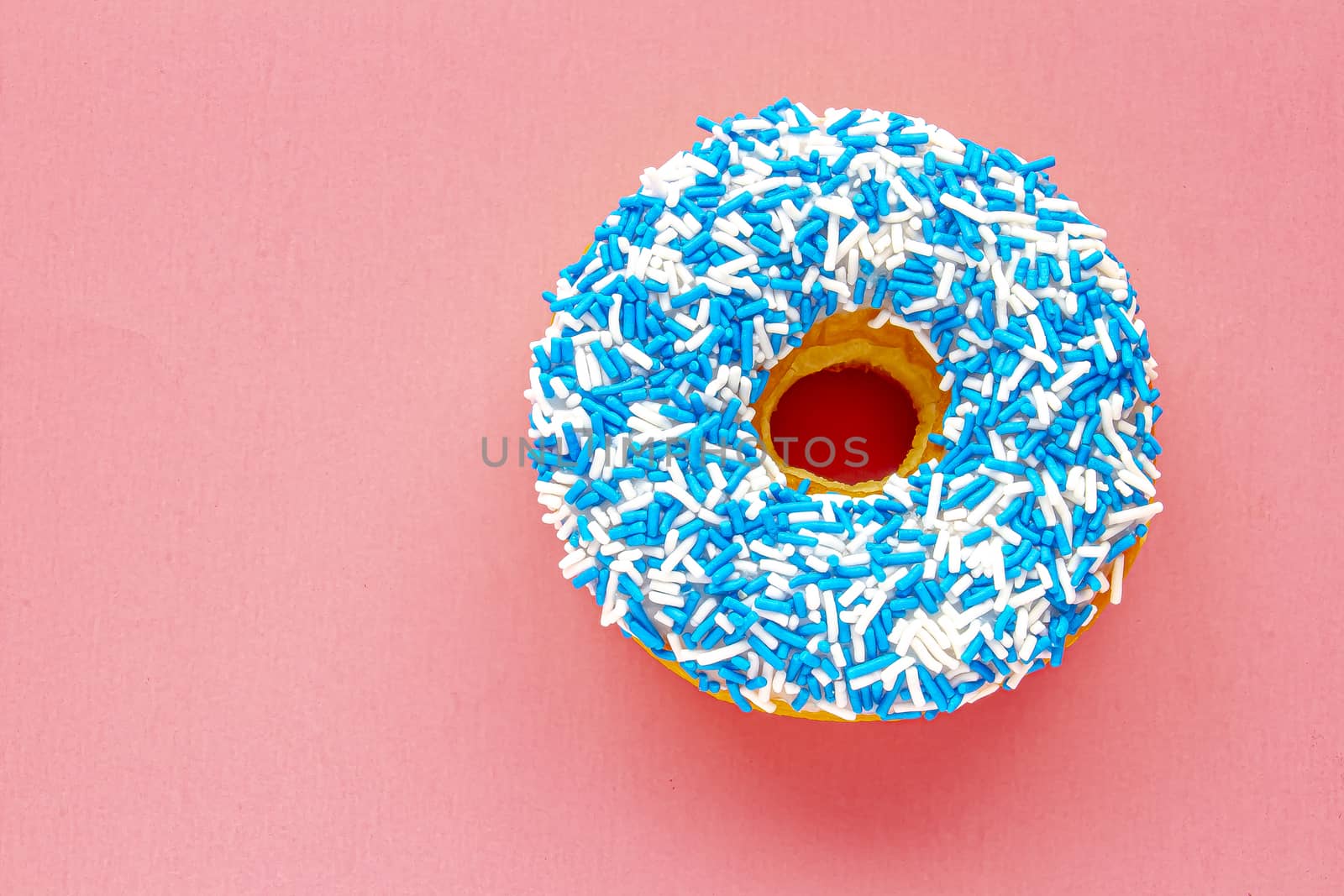 A Canadian Vanilla Dip Donut with Coloured blue and white Sprinkles on a pink background.