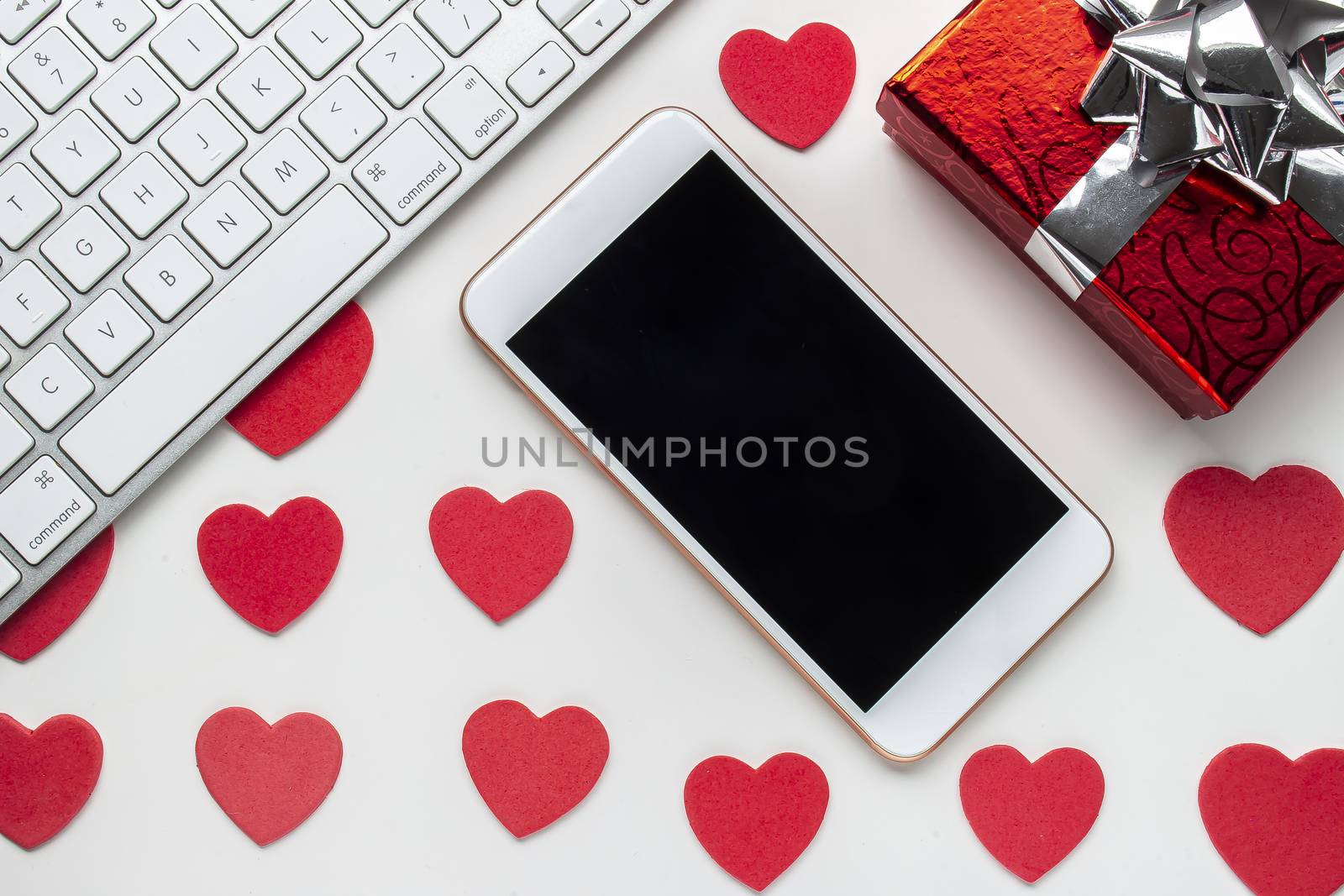 A smartphone with a keyboard and a red present and red hearts on a white background