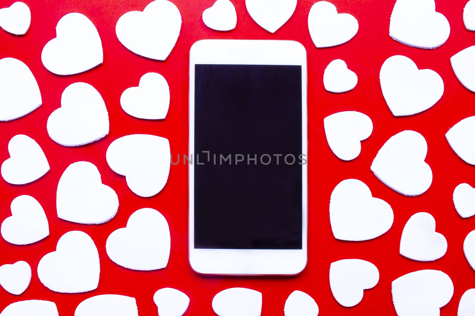 A smart phone surrounded by white hearts on a red background. Valentine’s Day