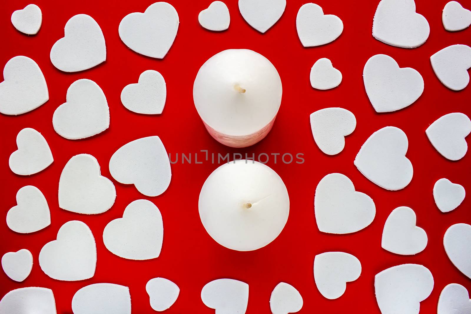 A couple of candles on a red background surrounded by white hearts
