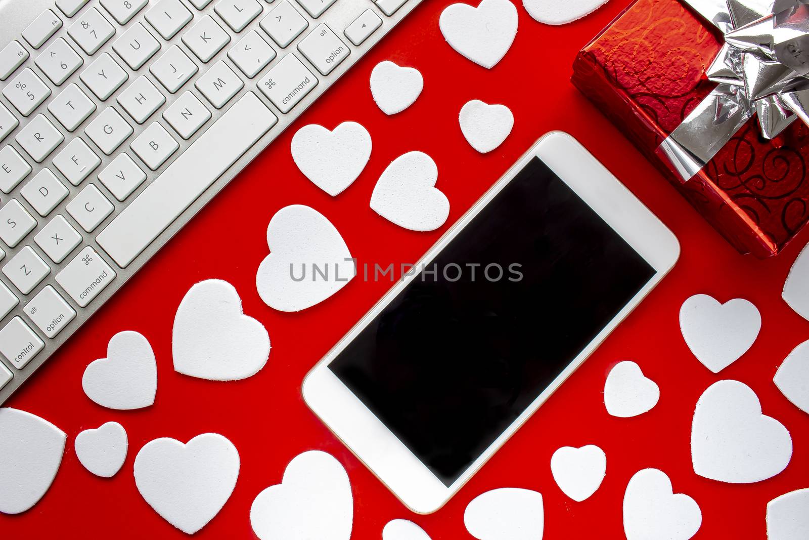 A smart phone with a keyboard a present and hearts on a red background with hearts by oasisamuel
