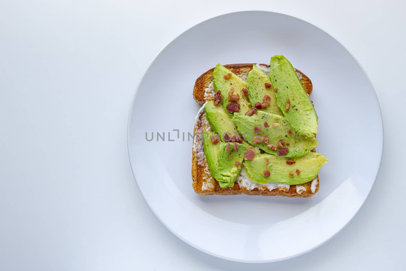 Full view of an avocado toast with bacon bites on a white plate