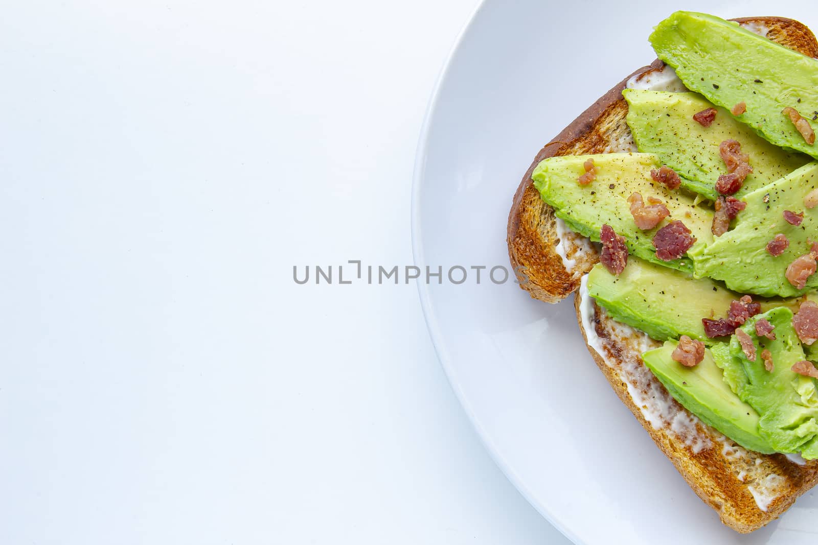 Close up of an avocado toast with bacon bites on a white plate on the right
