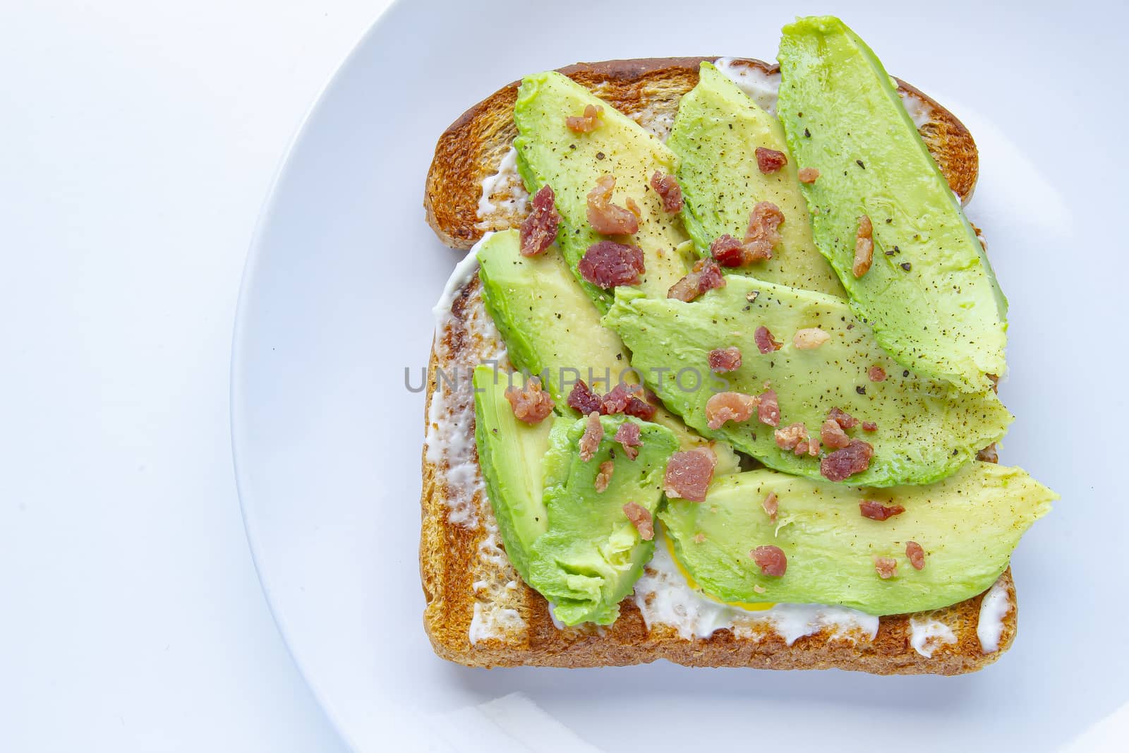 Close up of an avocado toast with bacon bites on a white plate