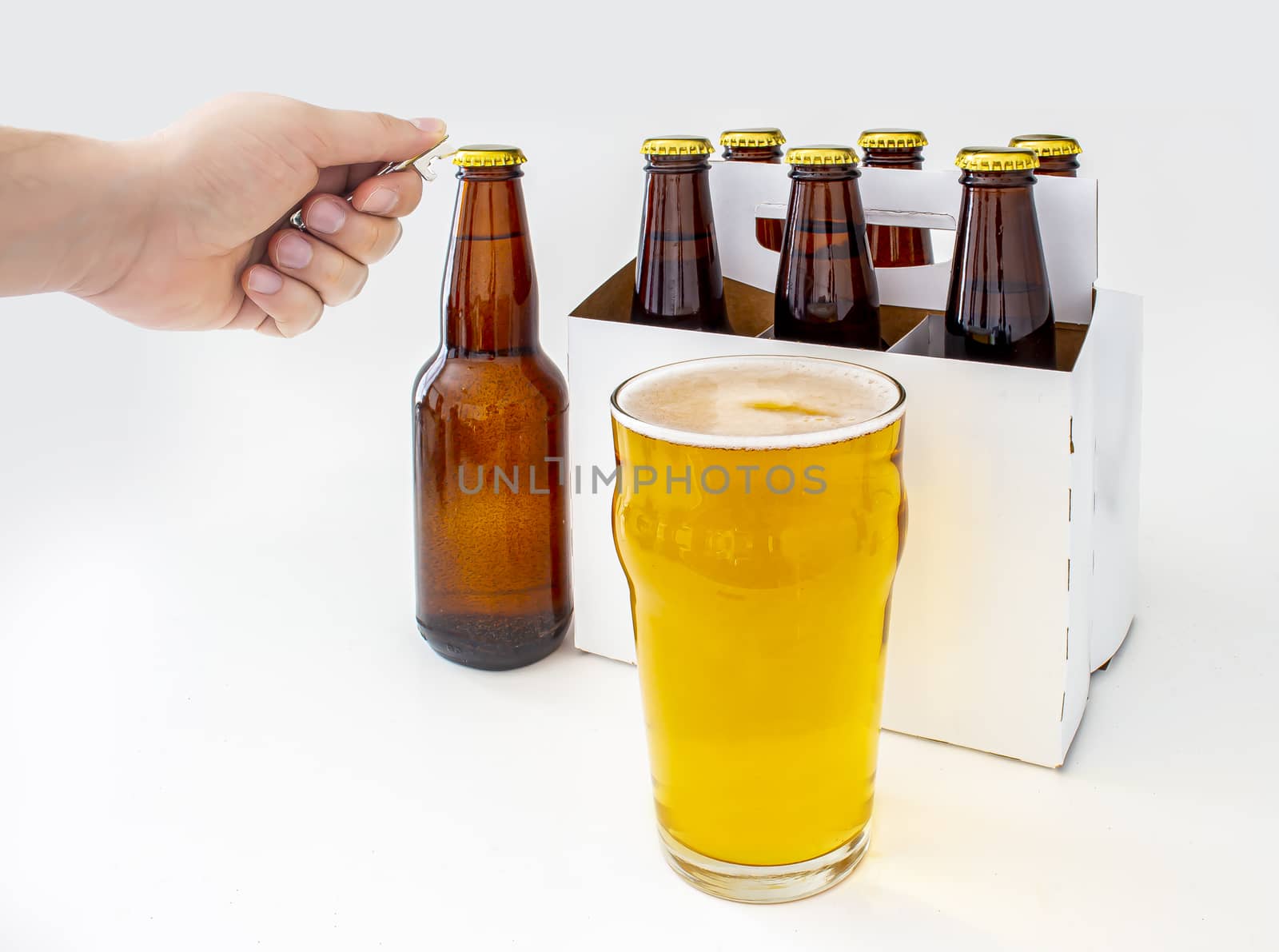 A person opening a Pilsner Style Lager brown bottle sic pack with a full pint of beer