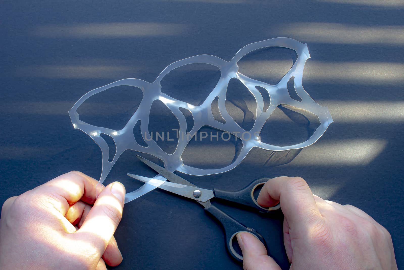 A person cutting a six pack rings or six pack yokes with scissors by oasisamuel