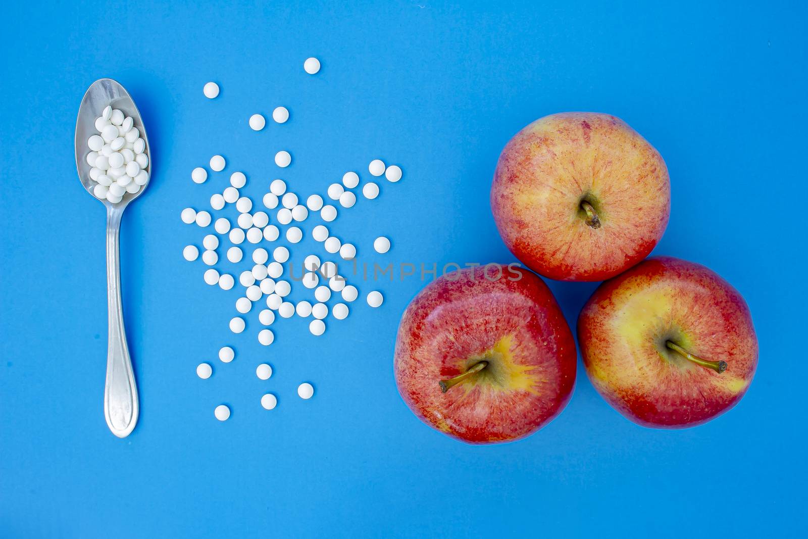 A spoon with supplements vitamins pills next to apples on a blue background