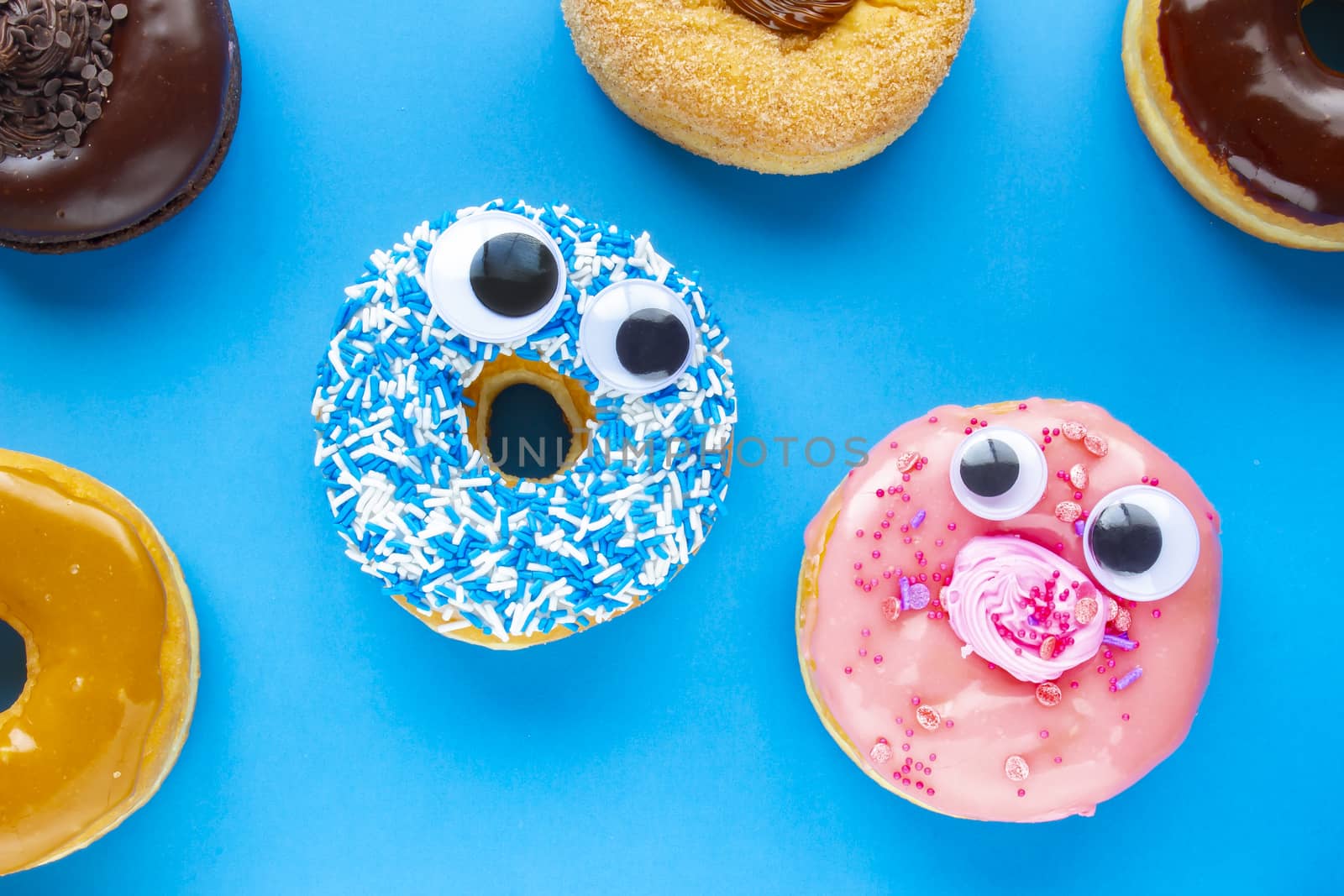 A blue donut with a pink donut with funny faces on a blue background looking each other