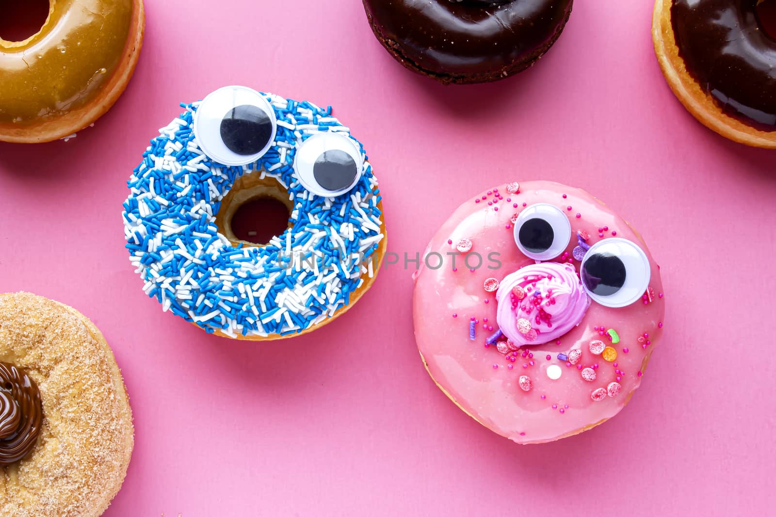 A blue donut with a pink donut with funny faces on a pink background looking each other by oasisamuel