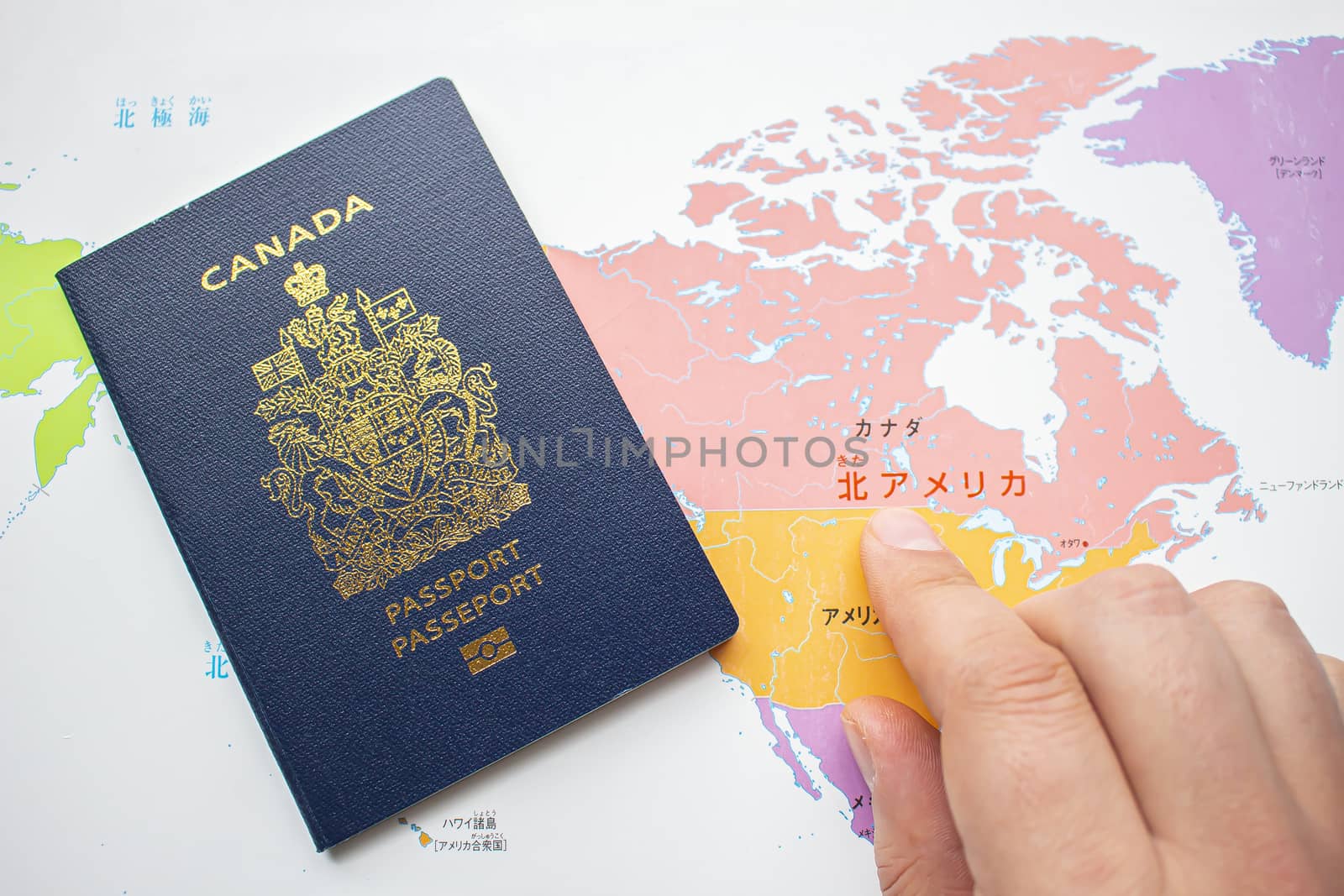 A Person's hand with a Canadian passport front cover on a map on the background
