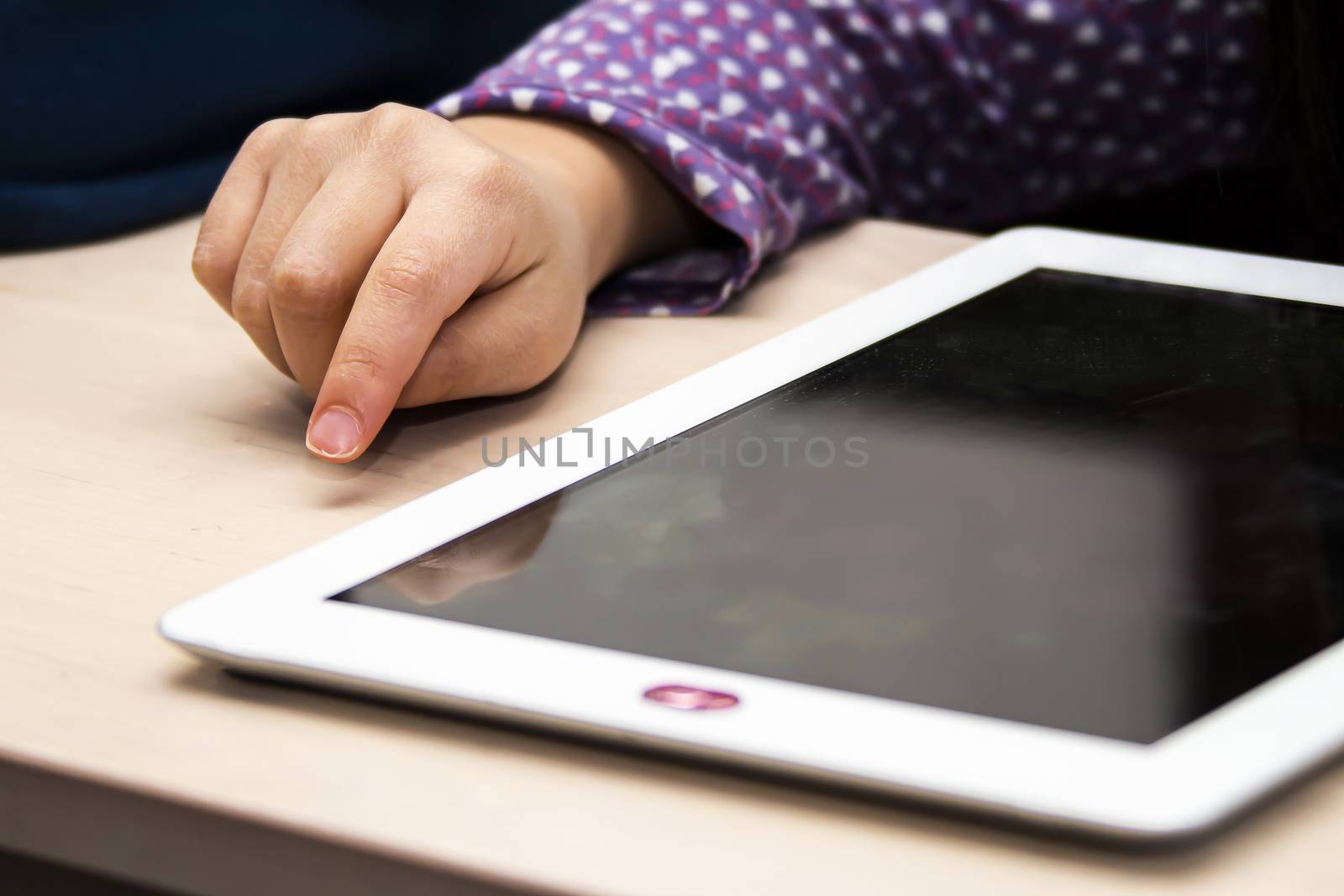 Close up front view of a little girl's hand using and white tablet with a privacy camera cover, during the day time