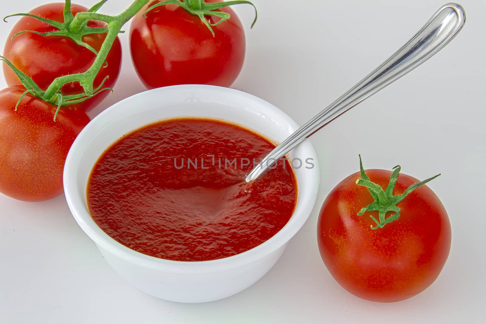 Fresh tomatoes sauce on a white plate with a spoon and  tomato berries on the side.