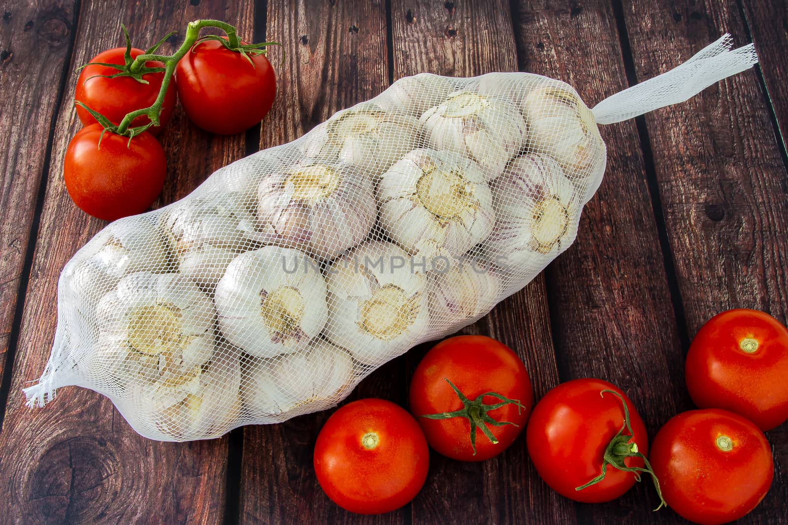 A bag of fresh garlic with tomatoes on a wooden table by oasisamuel